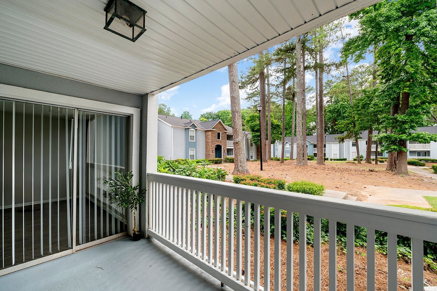Balcony view: White railing, trees, and apartment buildings on a sunny day at Mill House at East Cobb offers townhomes for rent in Cobb County.