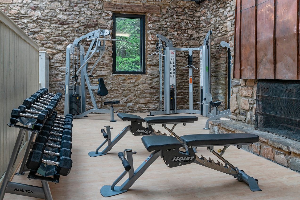 Gym with weights, machines, and benches against a stone wall with a window and fireplace at Mill House at East Cobb offers townhomes near Kennestone Hospital in Marietta, GA.