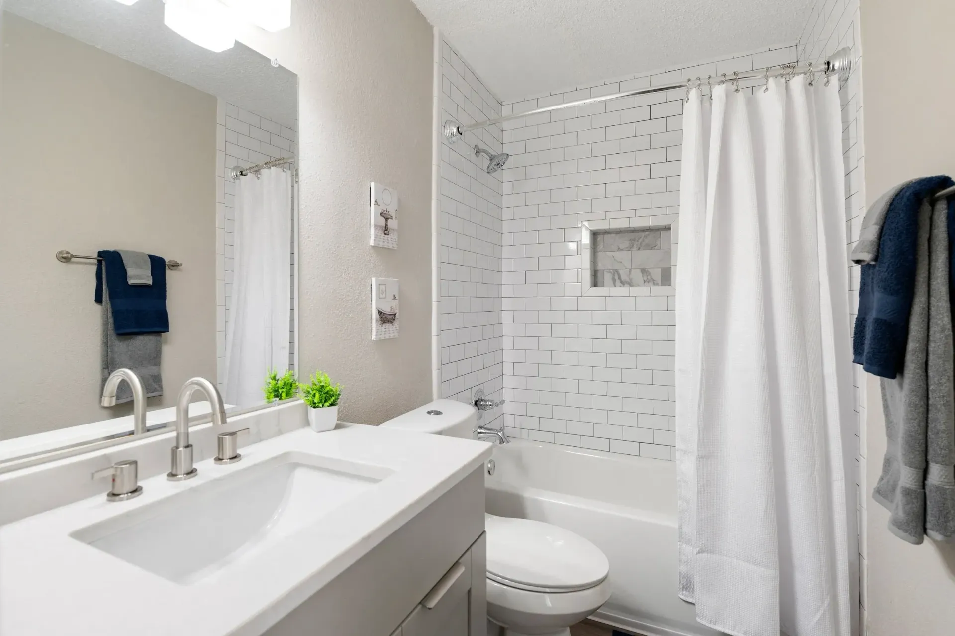 Bathroom with white fixtures, gray vanity, patterned shower wall, and blue towels at Mill House at East Cobb offers townhomes for rent in East Cobb, GA.
