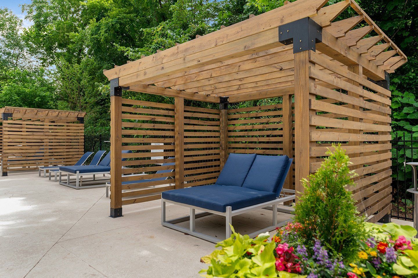 Lounge chairs under wooden pergolas on a patio, with a small flower bed at Mill House at East Cobb offers townhomes for rent in Marietta, GA.