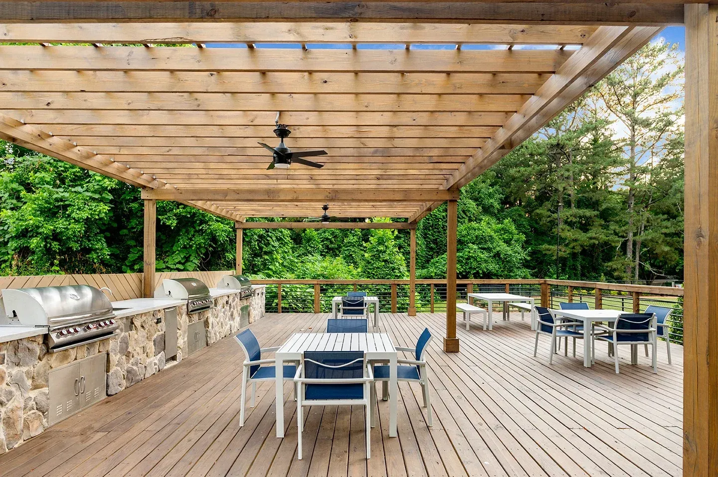 Outdoor deck with wooden pergola, grills, dining tables, and lush greenery backdrop at Mill House at East Cobb offers apartments in East Cobb, GA.
