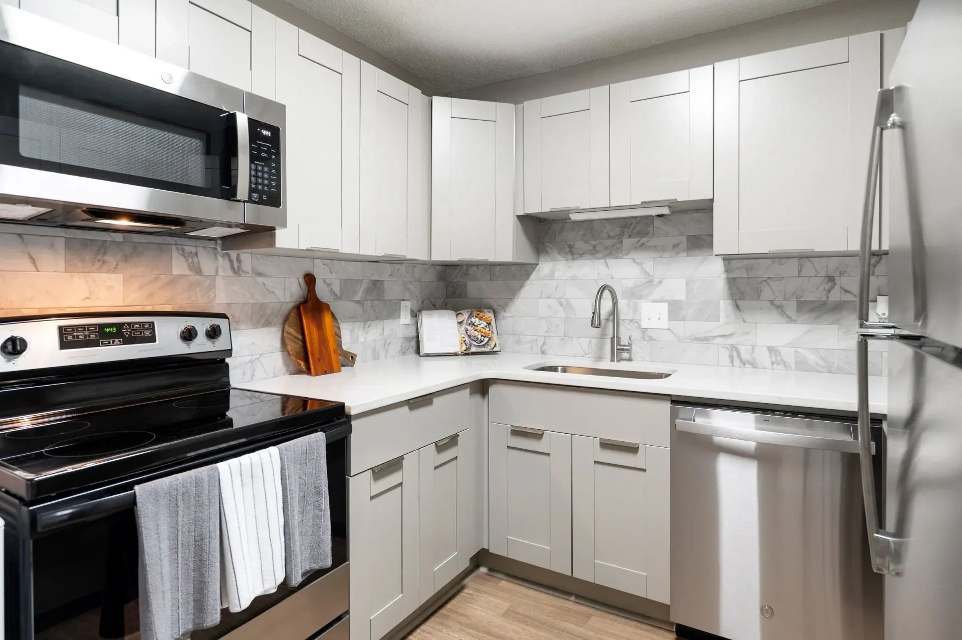 A modern kitchen with grey cabinets, stainless steel appliances, and white countertops at Mill House at East Cobb offers apartments in East Cobb, GA.
