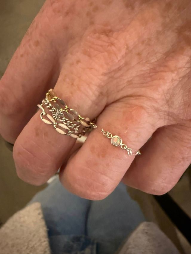 Close-up of a hand wearing two delicate gold rings, one with a chain-like design.