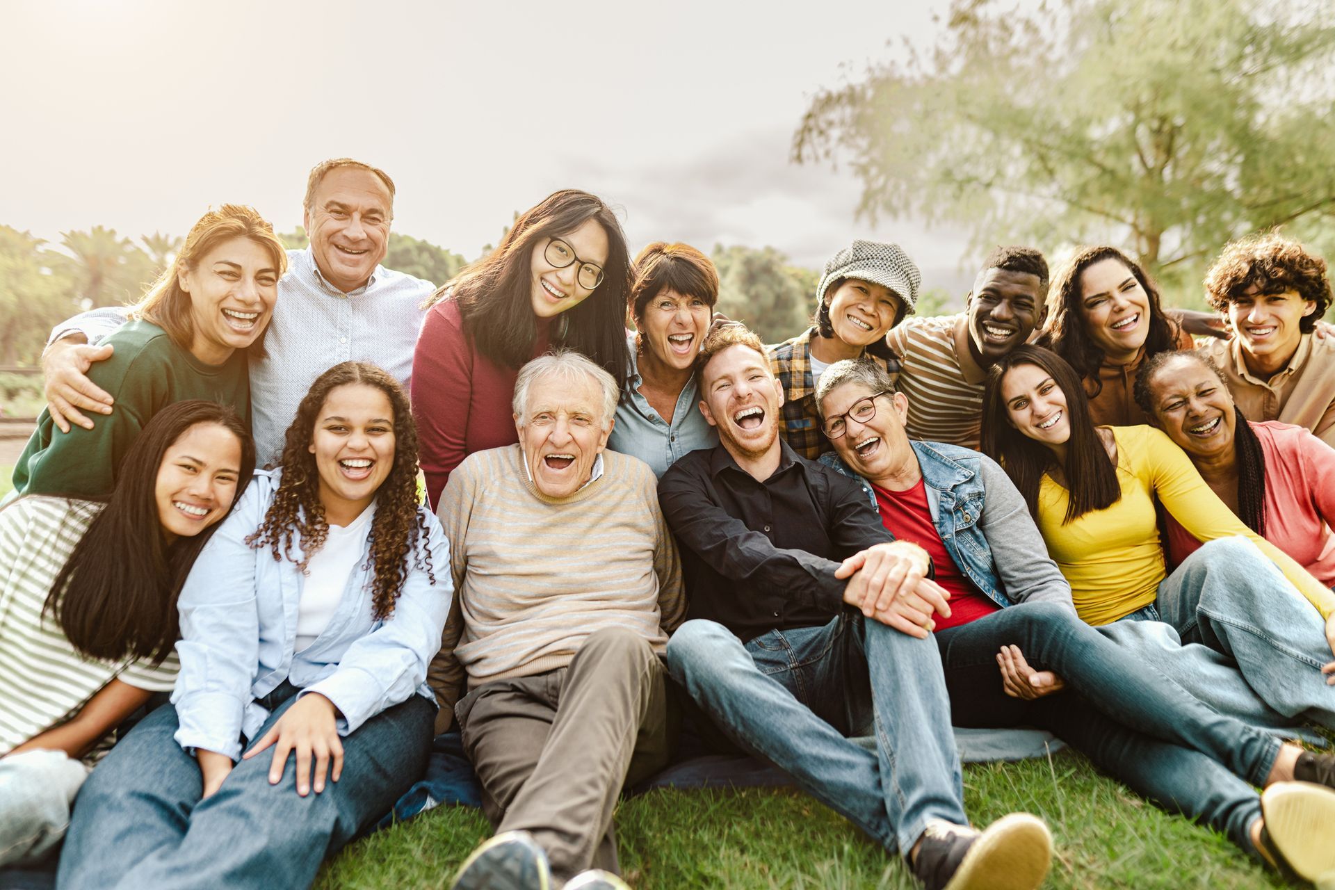 A large group of people are sitting on the grass in a park.
