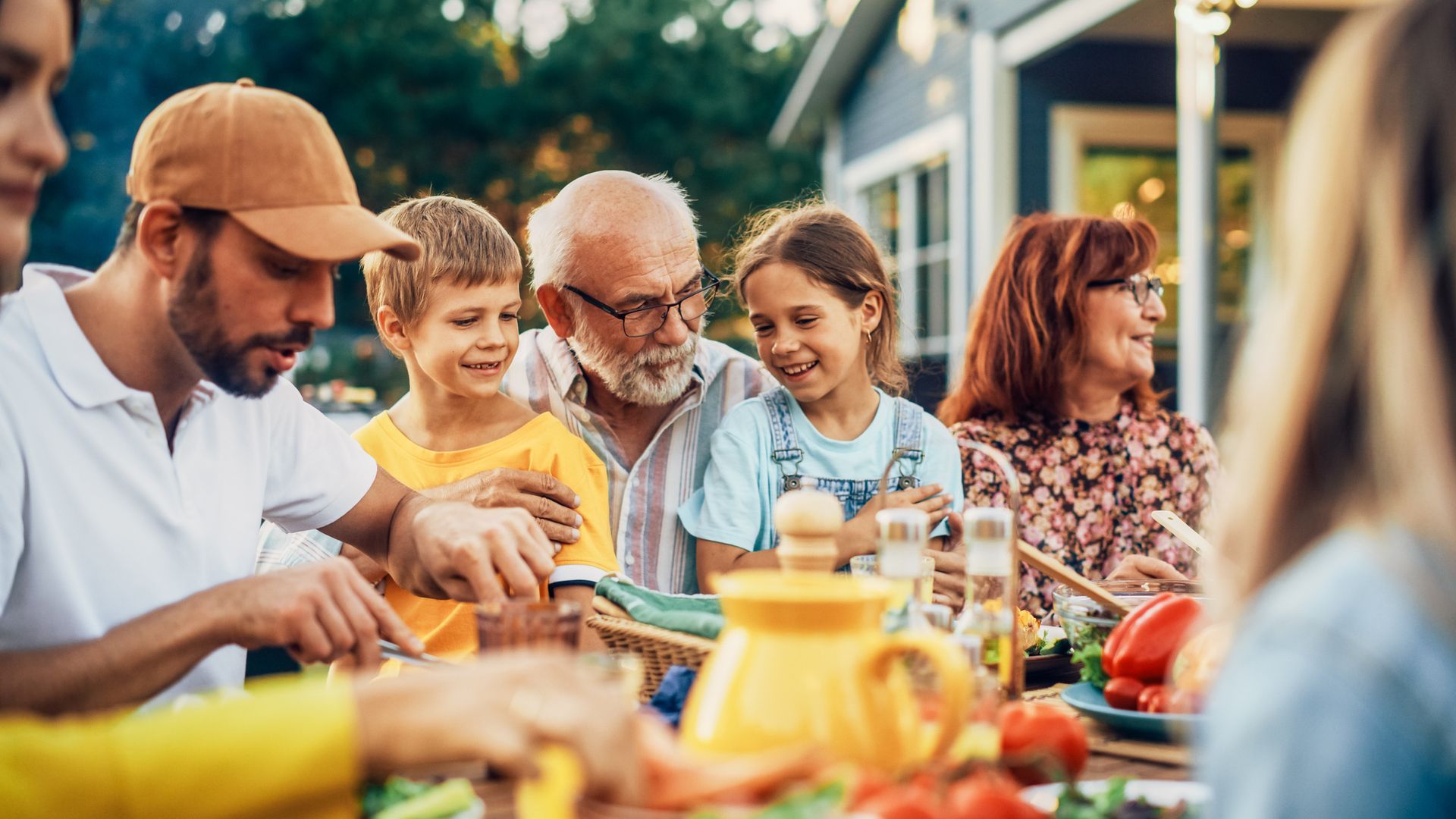 A large family is sitting around a table eating food.