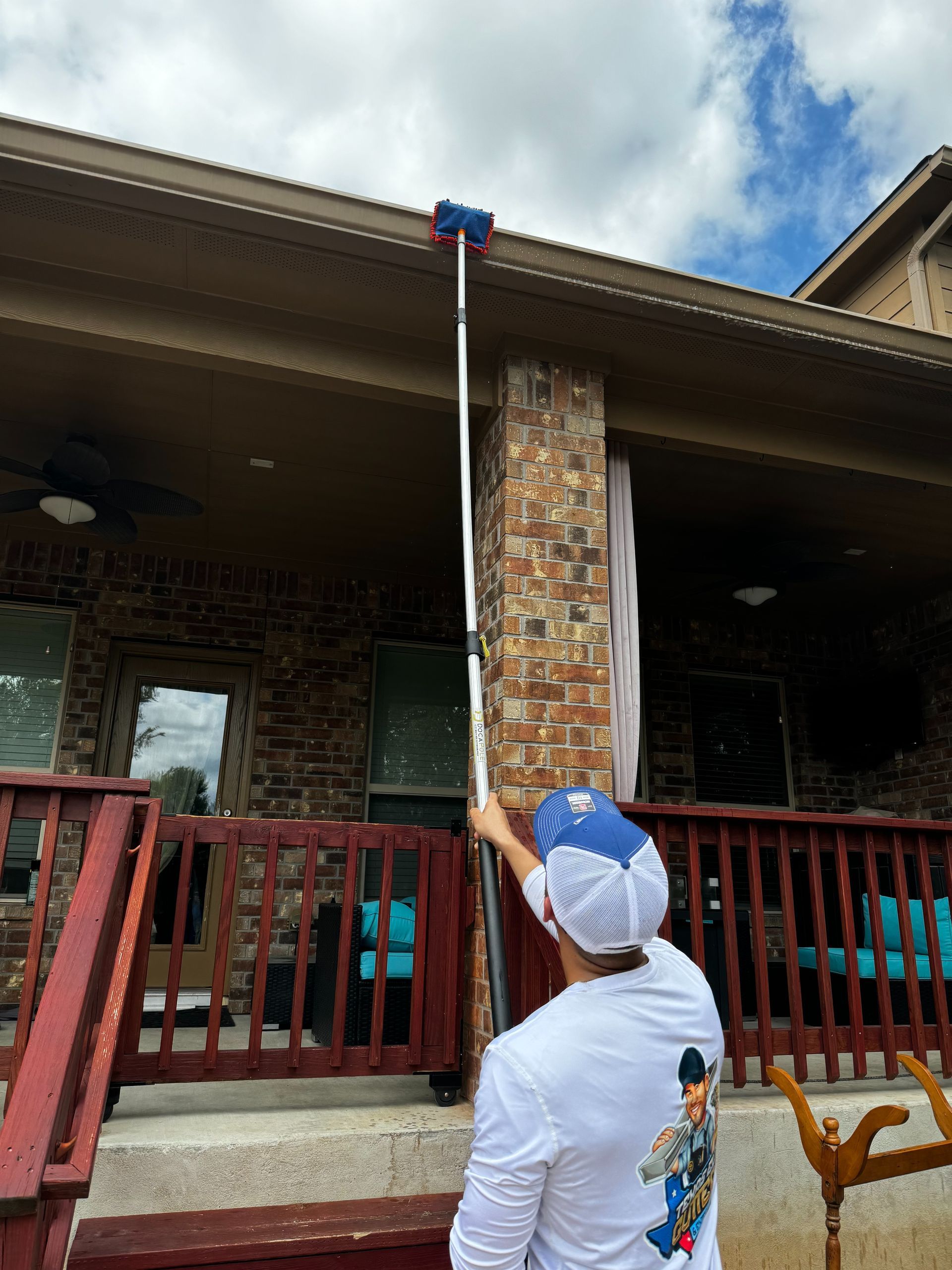 A man is cleaning the gutters of a house with a brush.