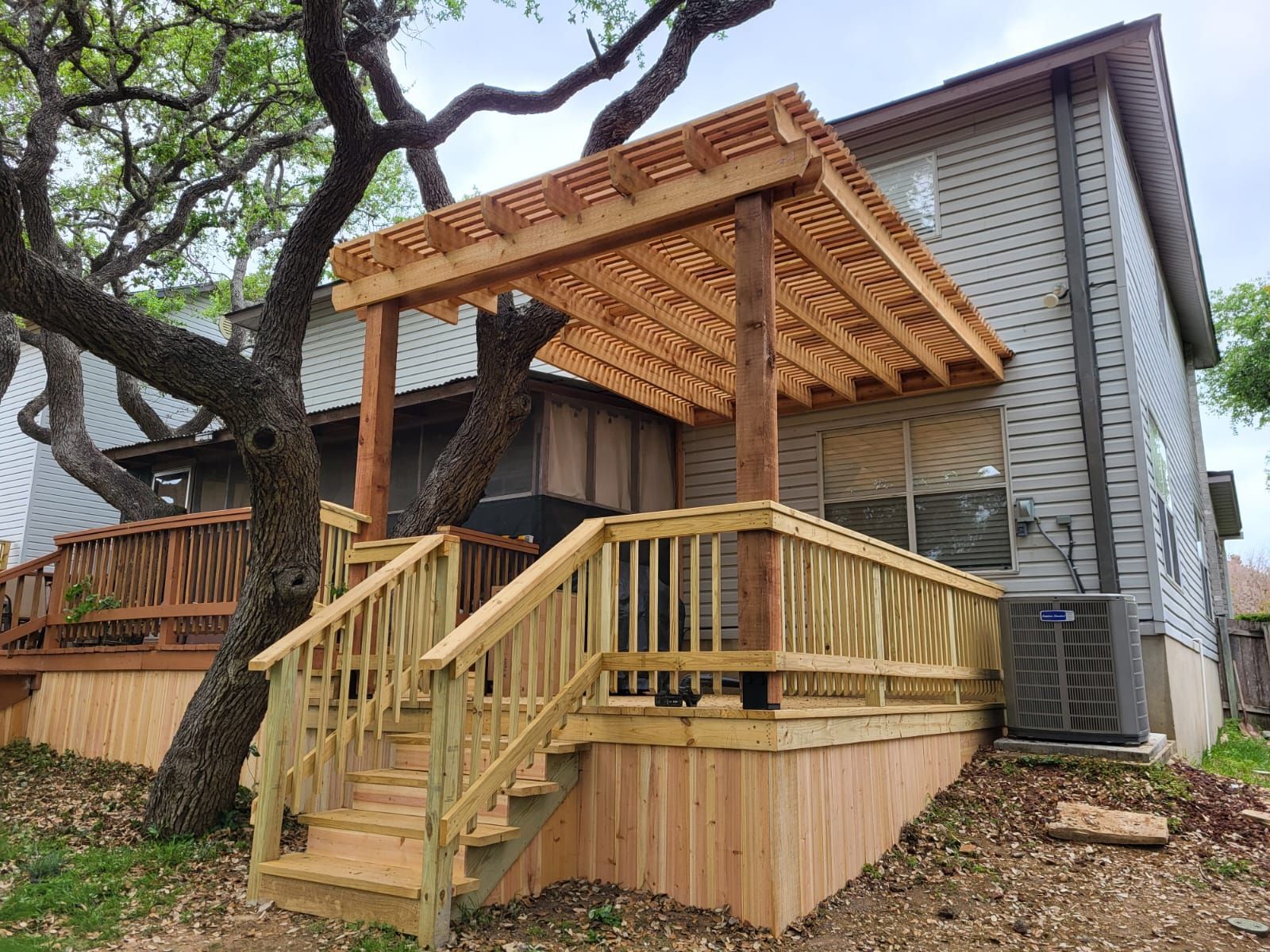 A wooden deck with stairs and a pergola in front of a house.