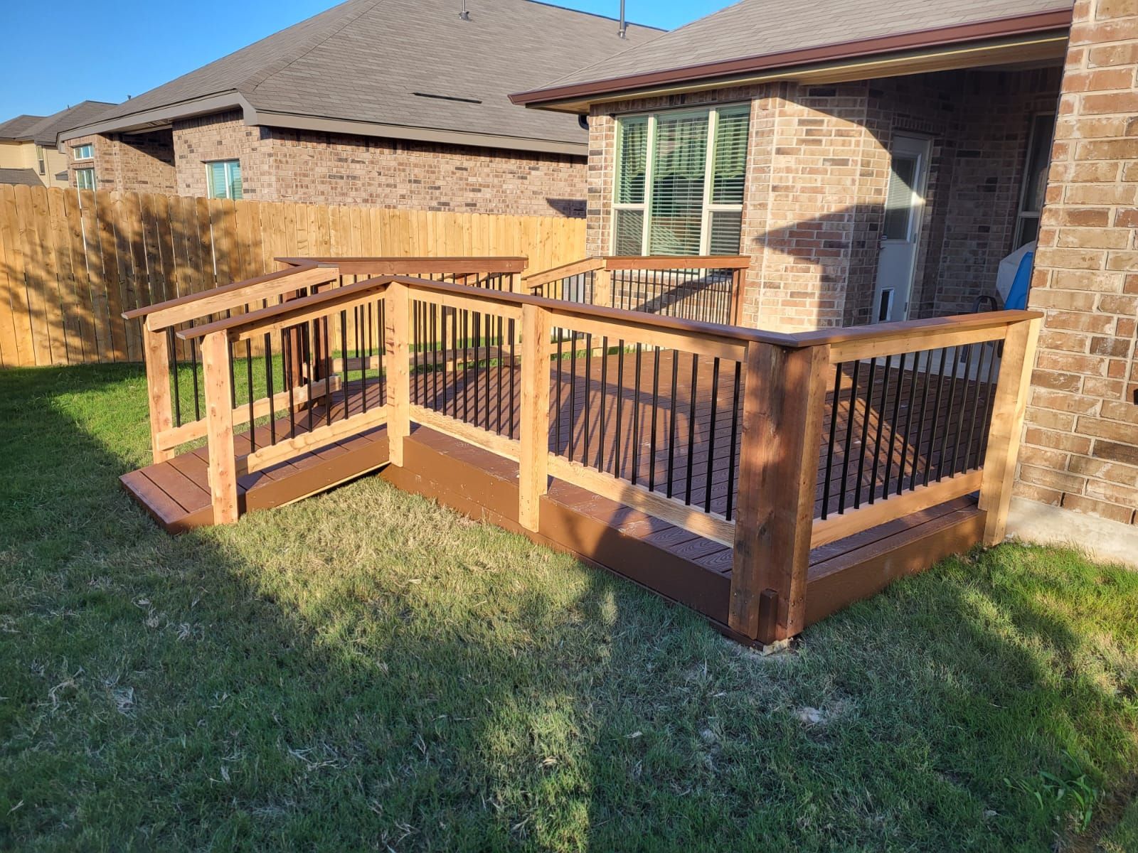 A wooden deck with a ramp in the backyard of a house.