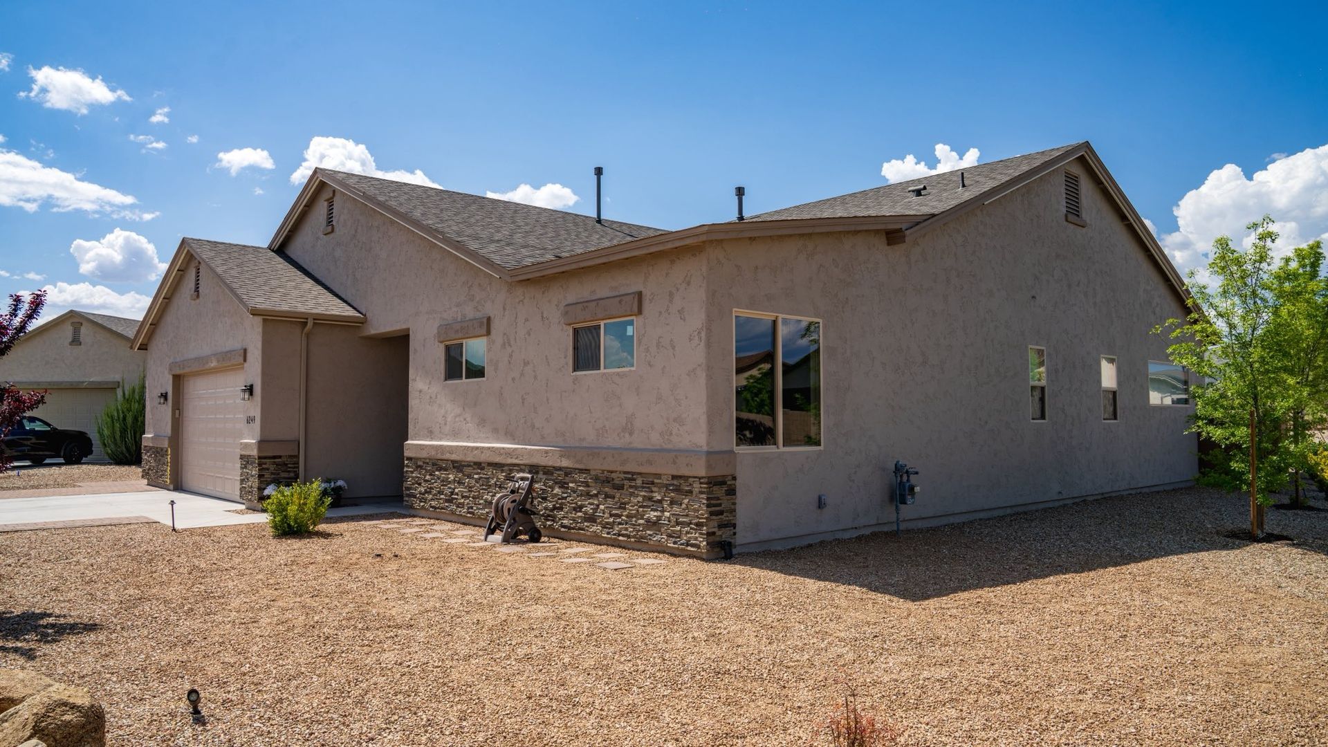 Tan stucco house with stone accents, gravel yard, and blue sky.