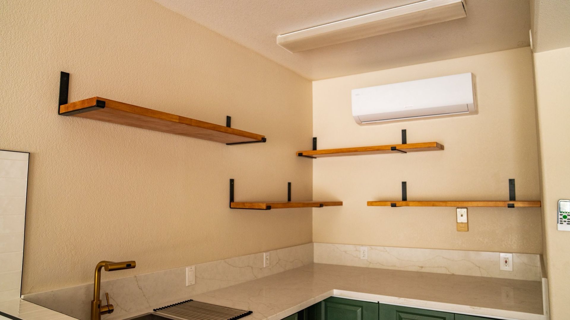 Wooden shelves mounted on black brackets above a countertop with a gold faucet and green cabinets.