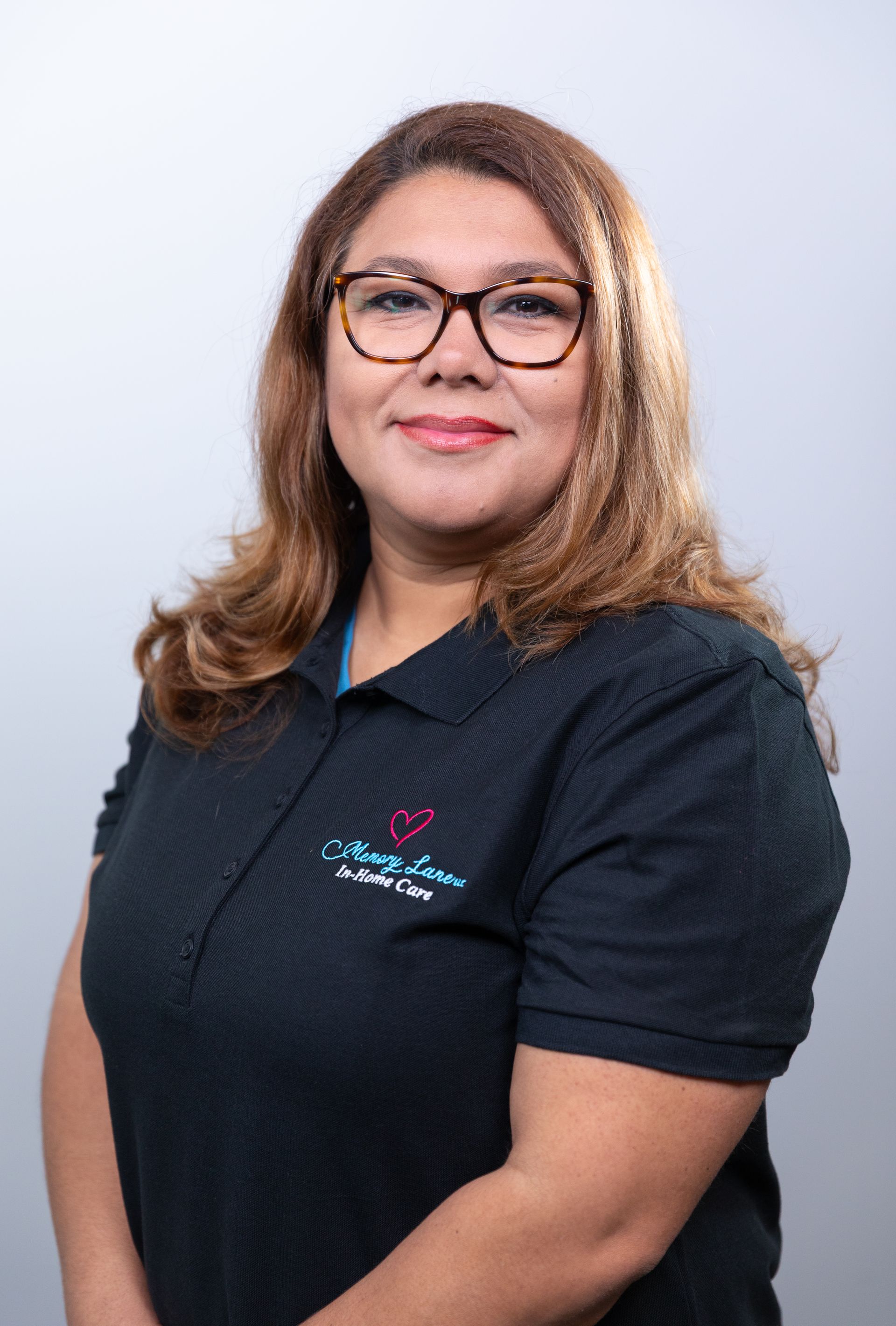 Woman with glasses wearing a black shirt with a logo, smiling, studio setting.