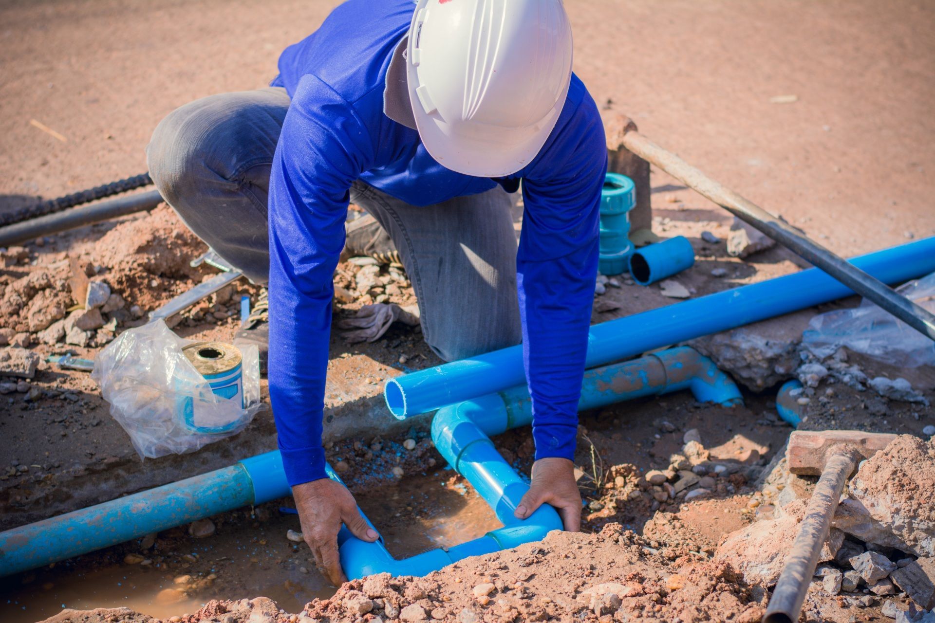 A man is working on a pipe in the dirt.