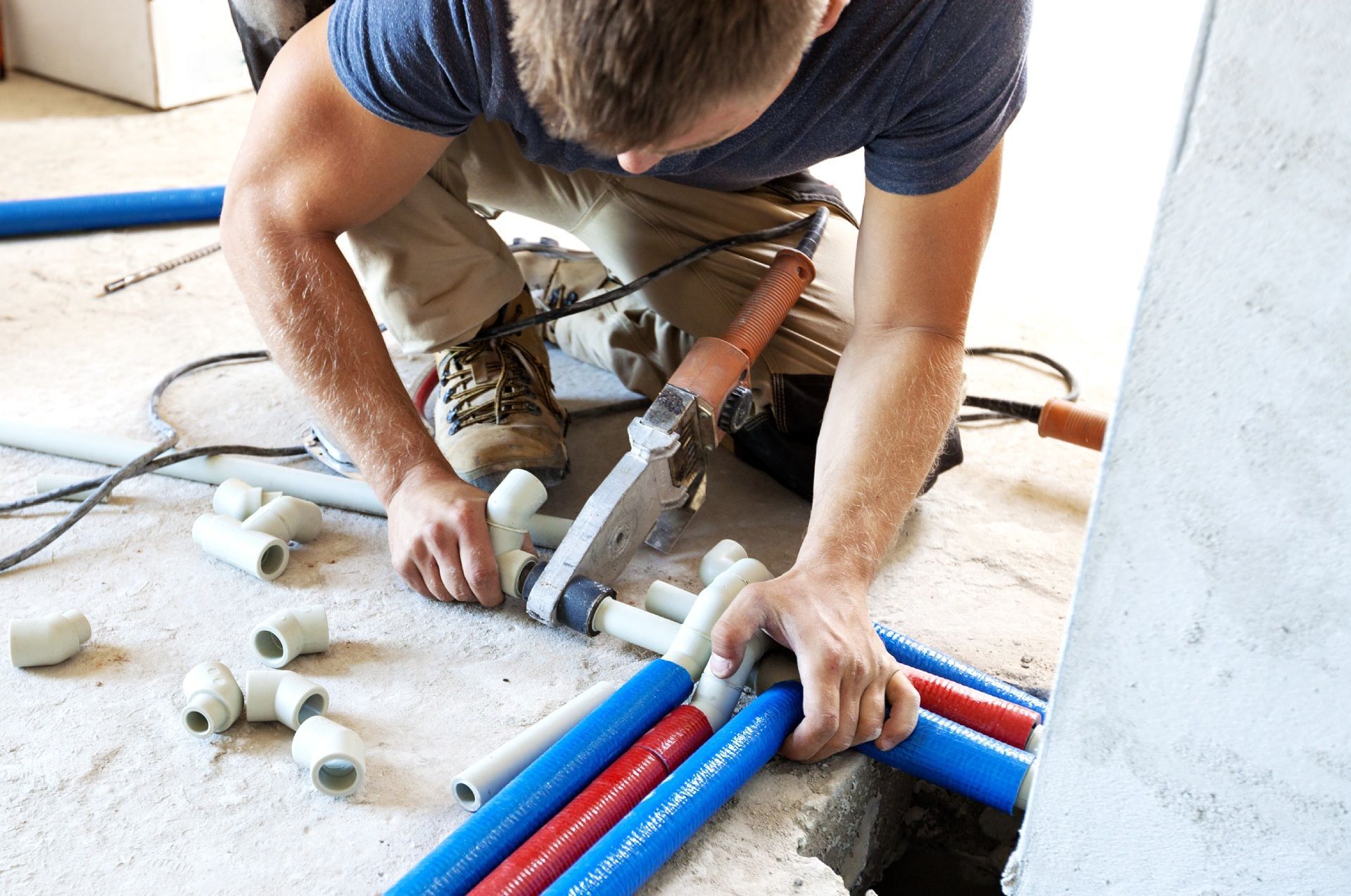 A man is kneeling on the floor working on pipes.