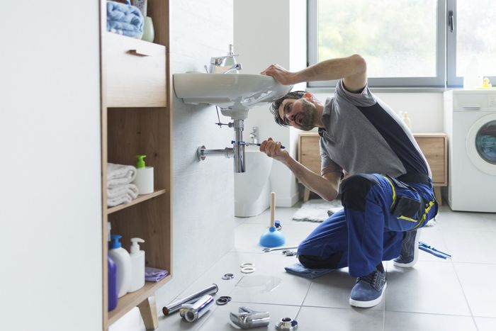 A plumber is fixing a sink in a bathroom.