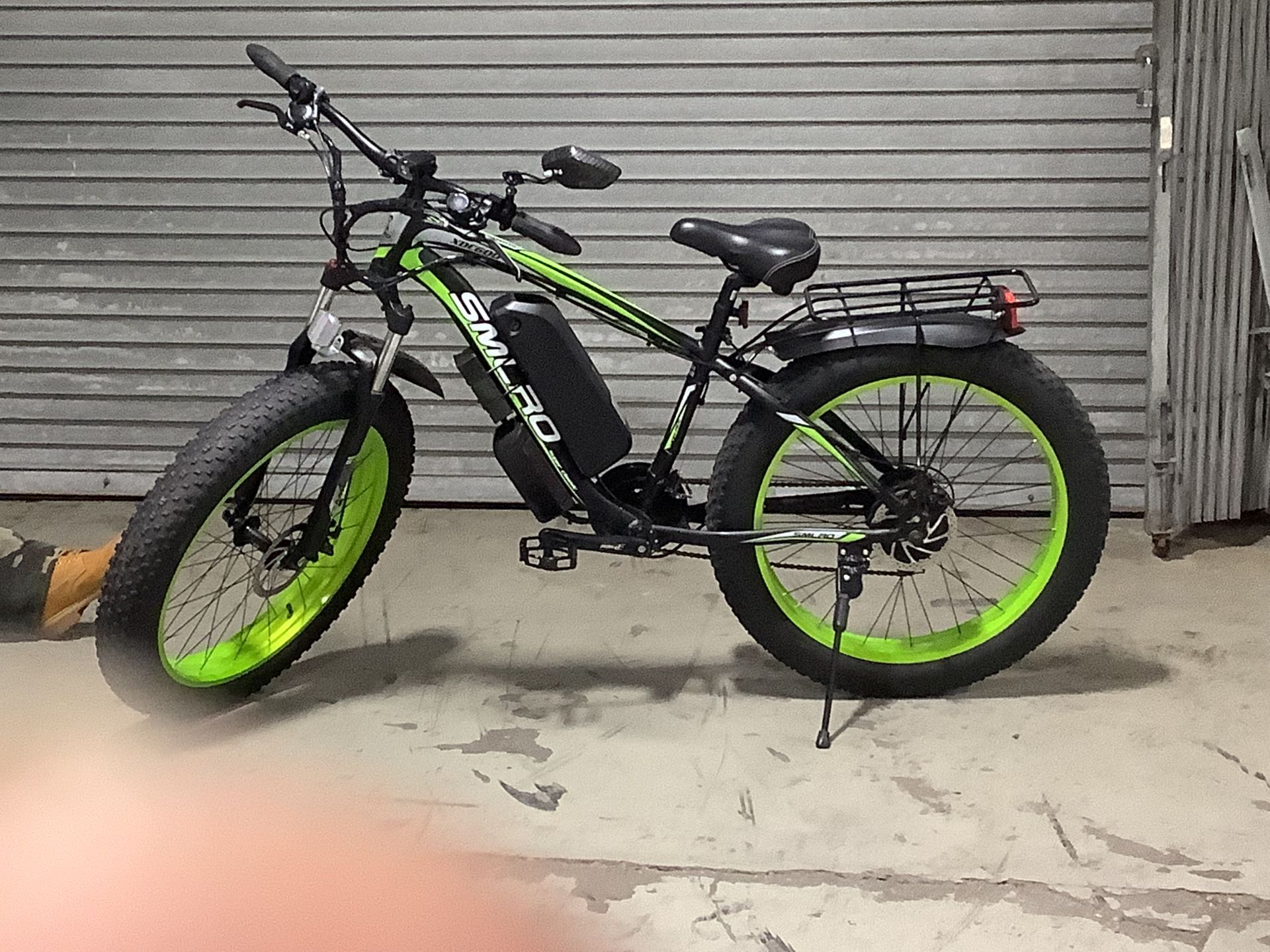 A green and black electric bike is parked in front of a garage door.