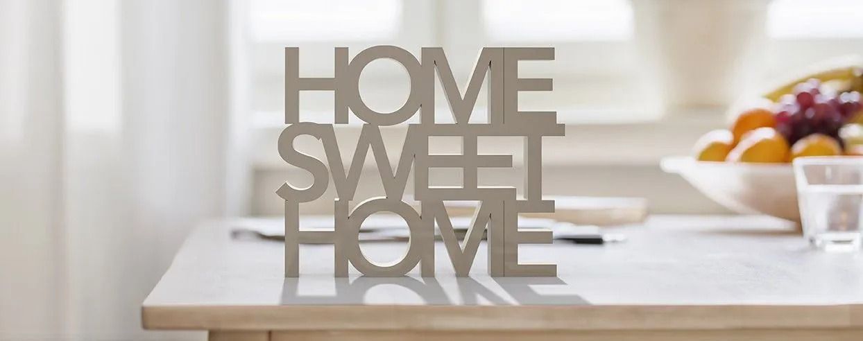 Decorative “Home Sweet Home” sign on a bright kitchen countertop with fruit in the background