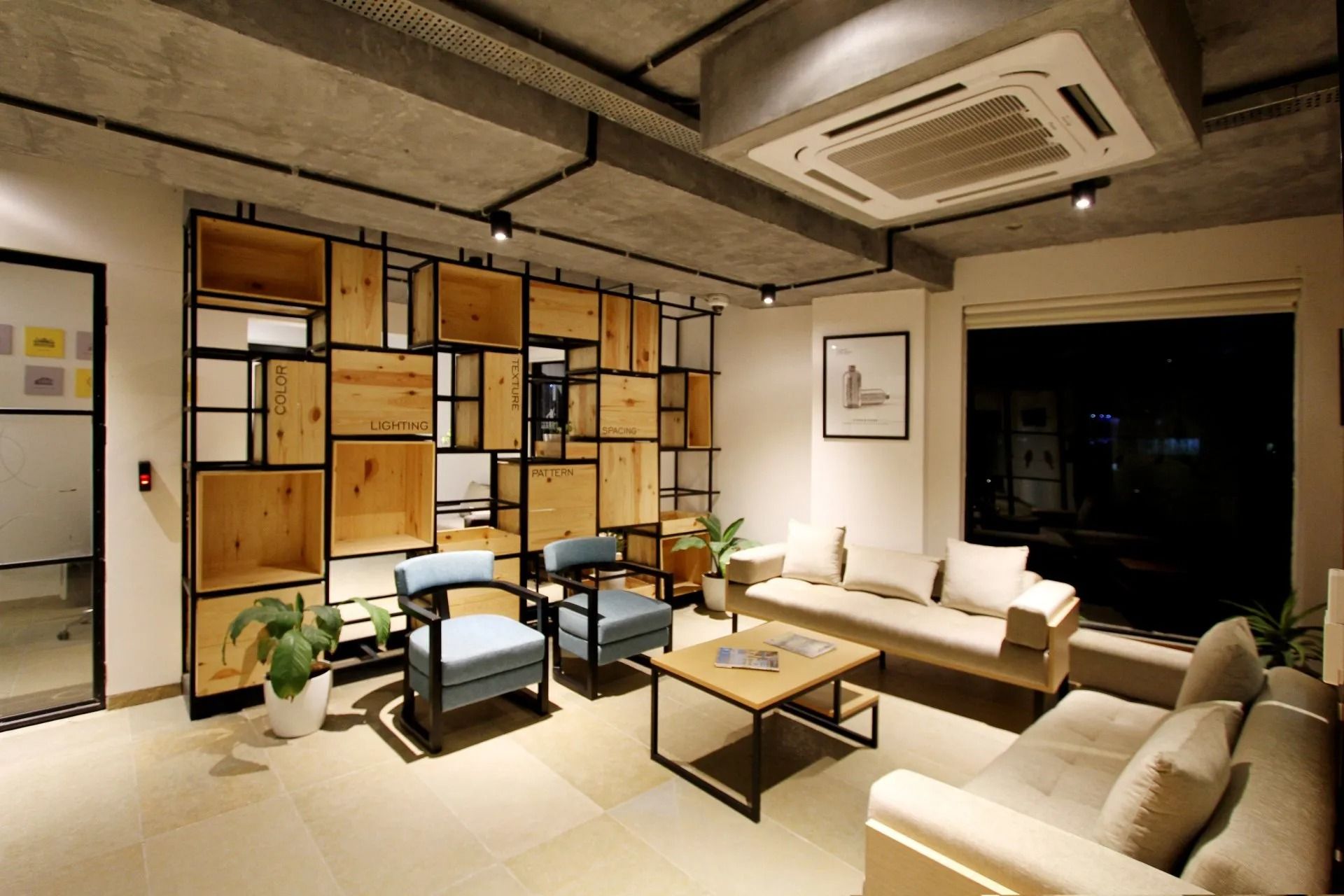 Modern living room with beige sofas, coffee table, plants, and a black metal shelving divider against warm lighting