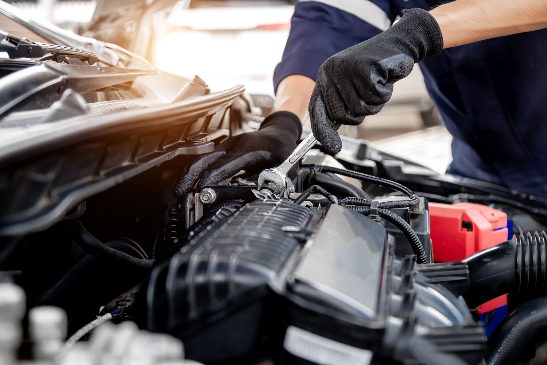Mechanic with black gloves works on a car engine, using a wrench. Close-up shot.