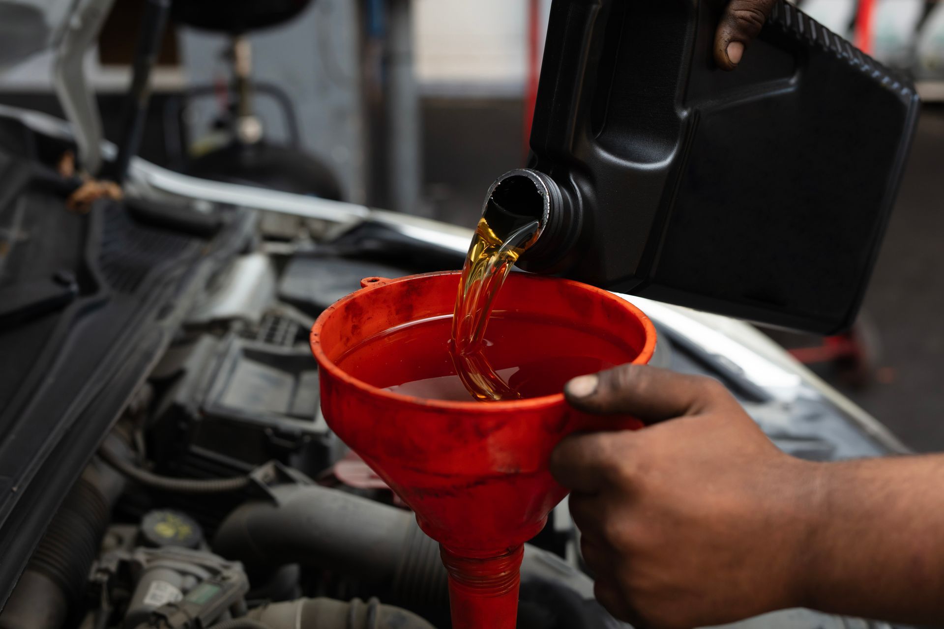 Person pouring oil into car engine using a funnel.