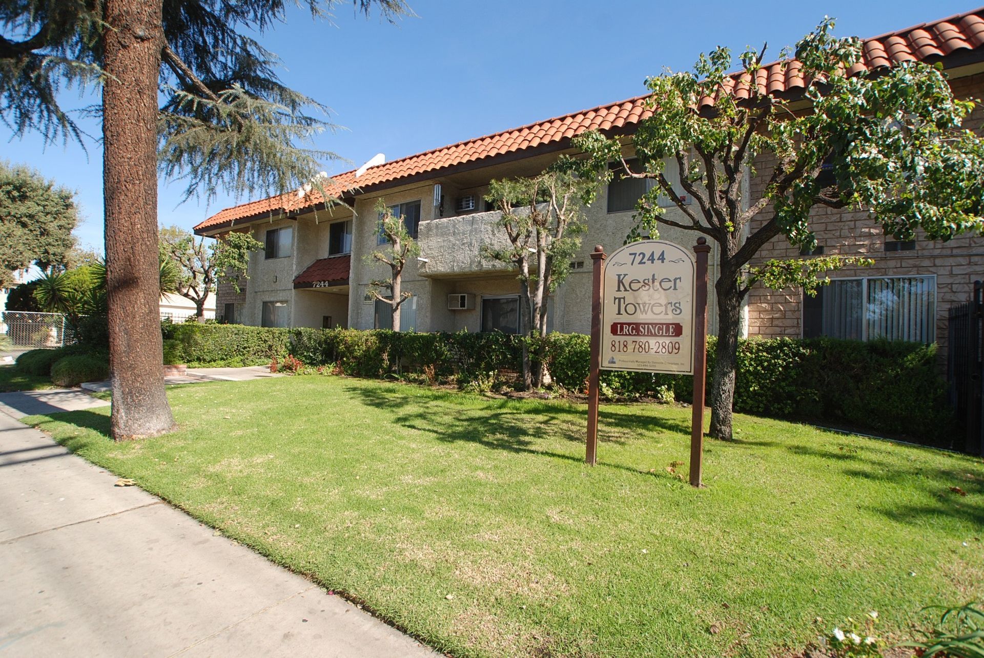 Apartment building with orange tile roof, sign, and green lawn.