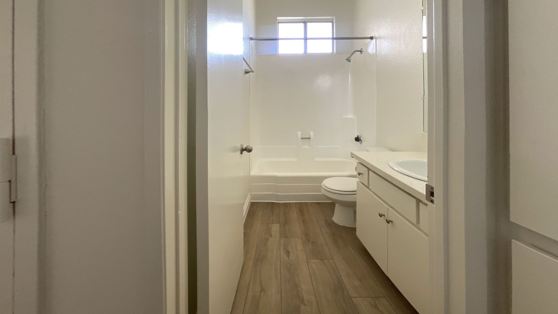 Bathroom with white walls, a bathtub, toilet, vanity, and wood-look flooring.