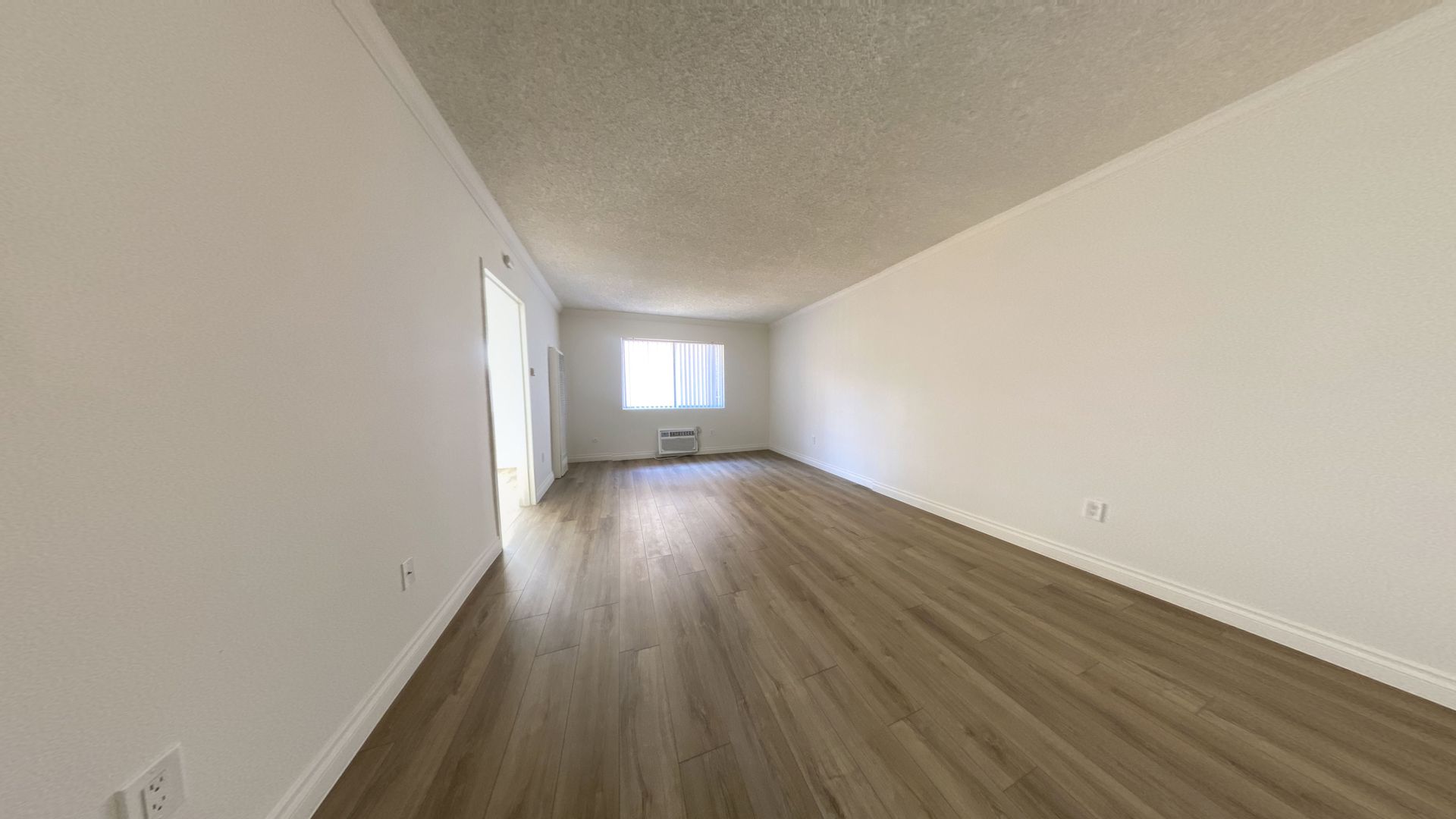 Empty room with light wood floor, white walls and ceiling, window, and sliding door.
