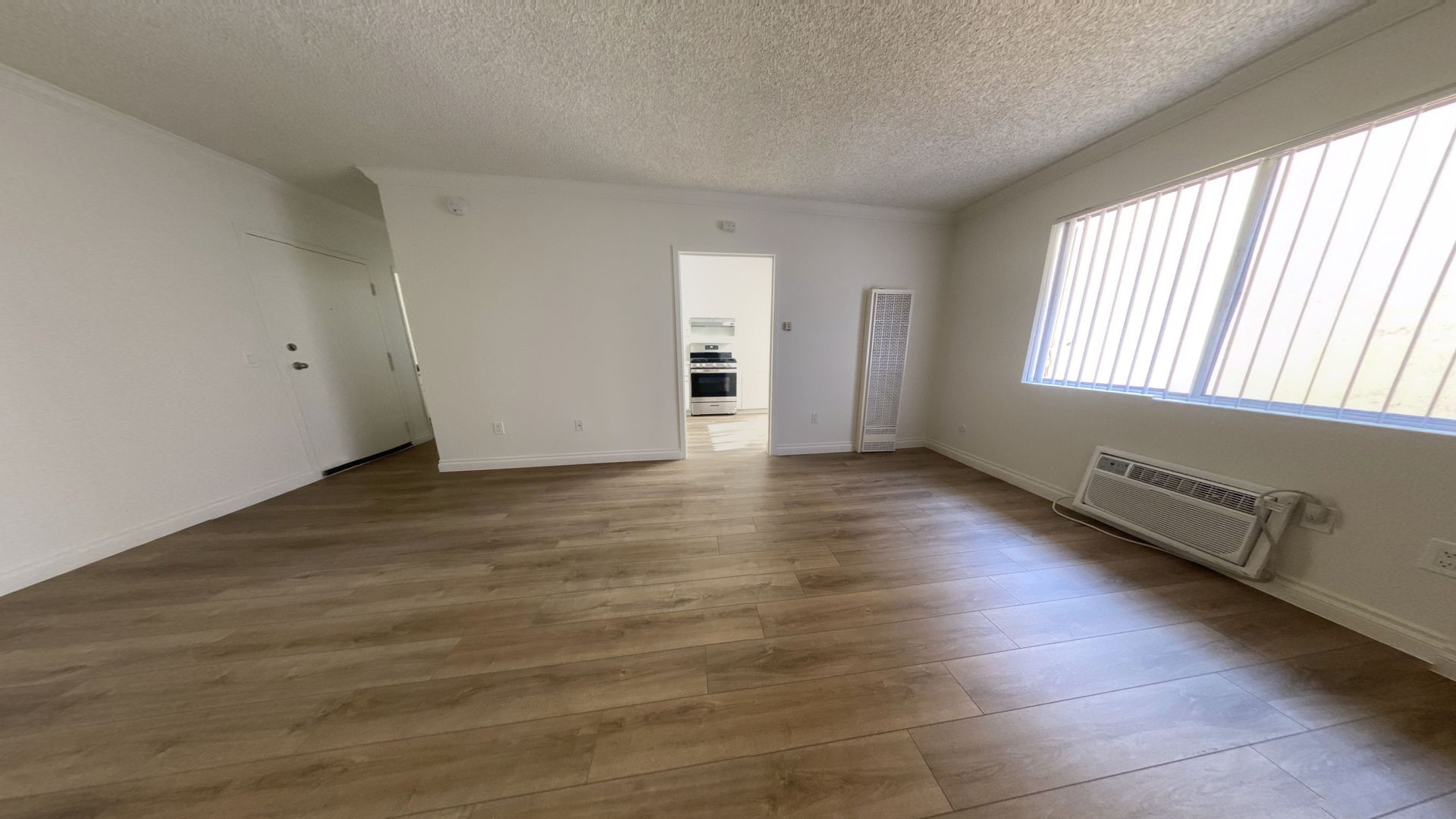 Empty room with wood-look floor, white walls, and a view into a kitchen.