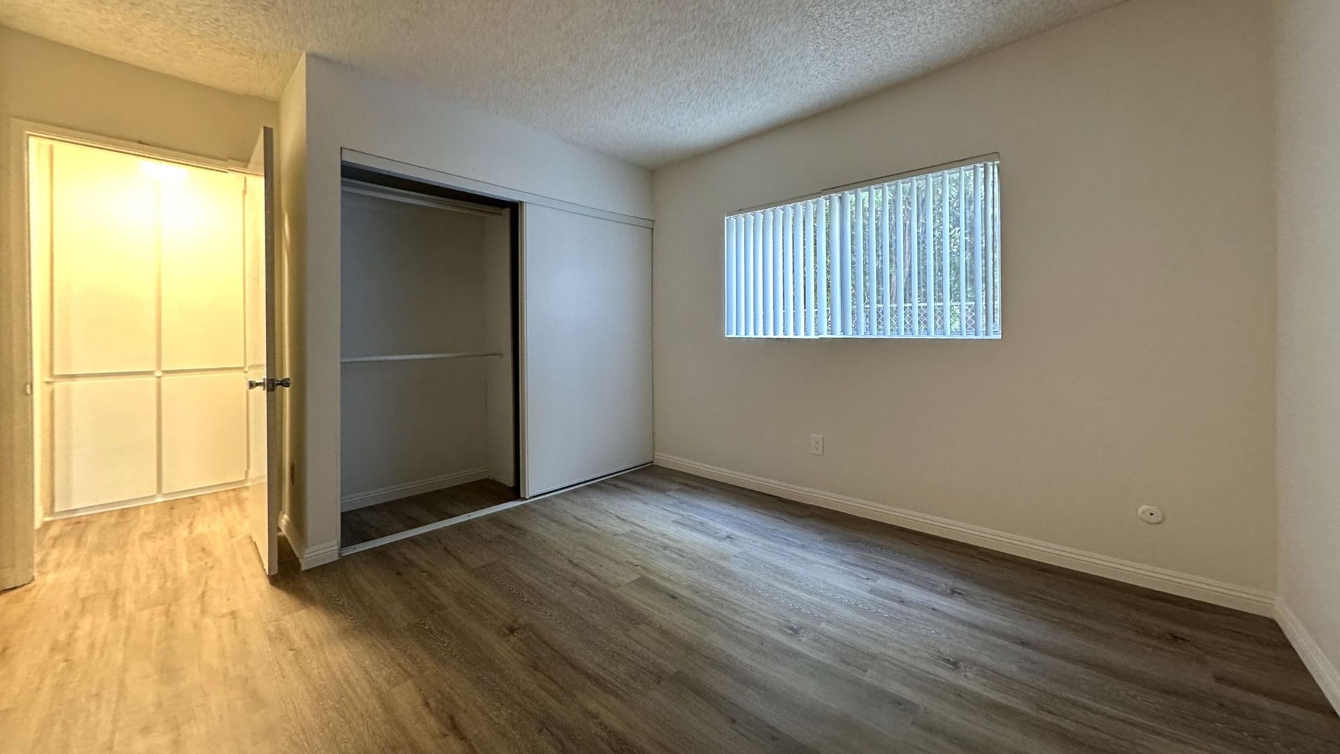 Empty bedroom with closet and window; wood-look floor, light walls, and a ceiling.