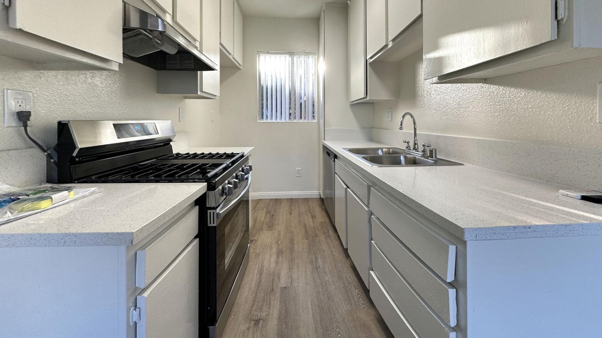 Kitchen with white cabinets, countertops, and appliances. Has a gas stove, sink, and window.
