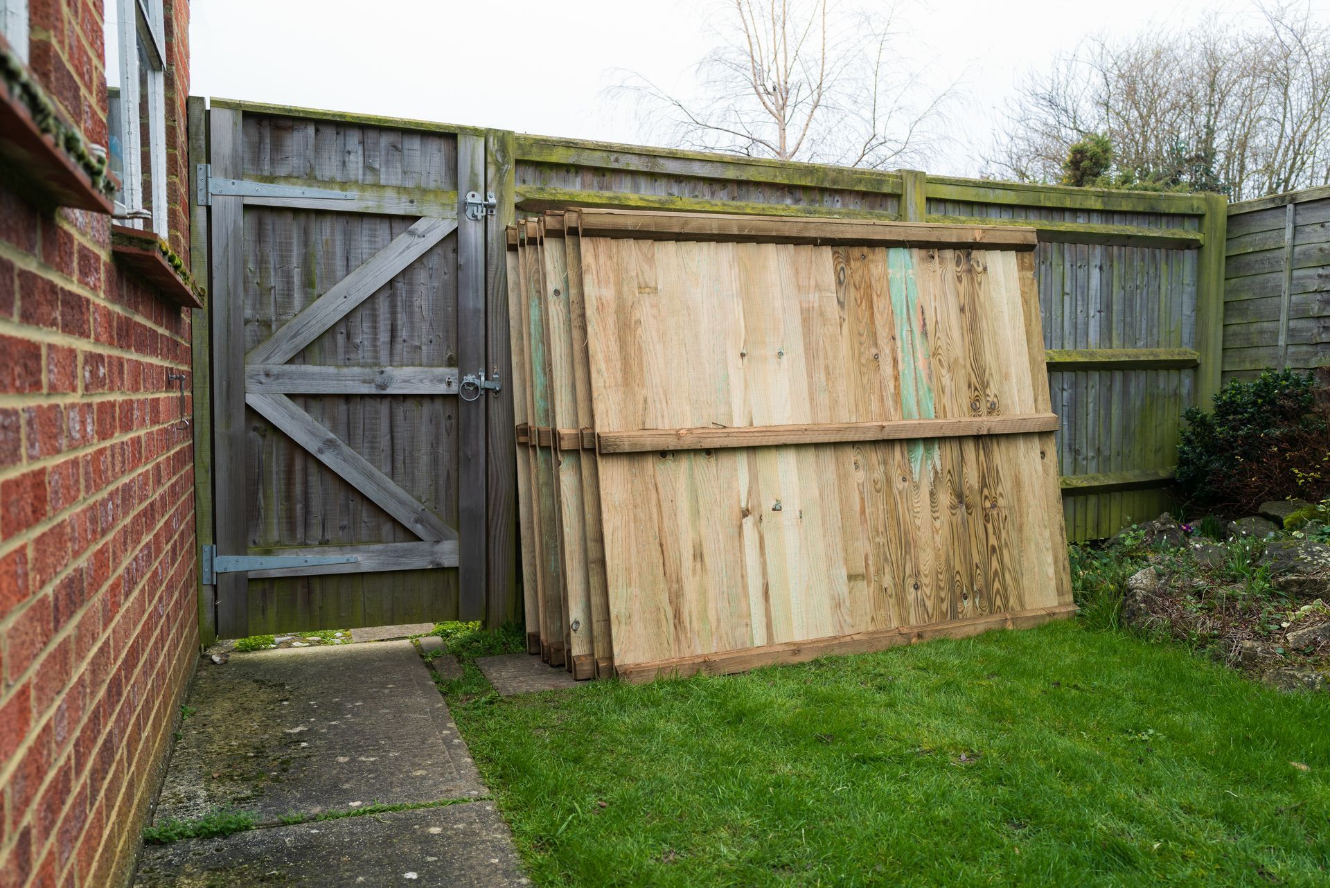 Stack of vertical slat replacement fence panels in a residential backyard, prepared for installation.