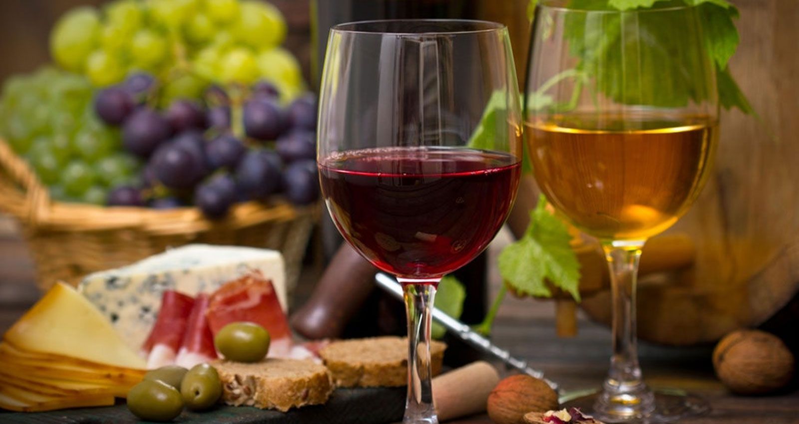 Dos copas de vino están sobre una mesa junto a una cesta de uvas.