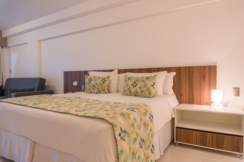 Una habitación de hotel con una cama king size, mesita de noche y sofá.