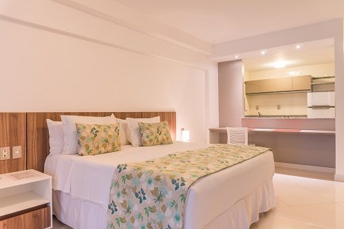 Una habitación de hotel con una cama king size y una cocina al fondo.