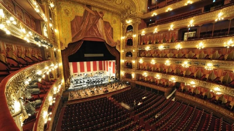 El interior de un gran teatro con asientos rojos y un escenario.