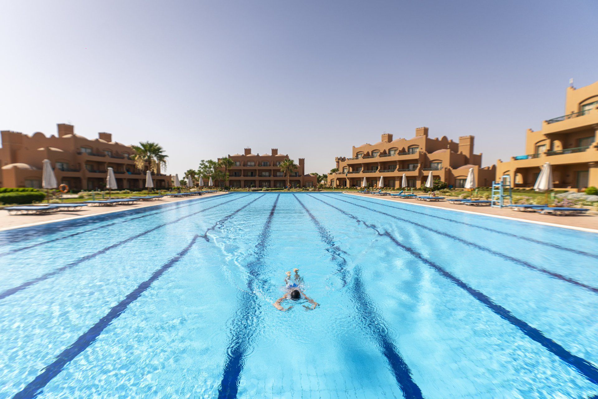 A man is swimming in a large swimming pool surrounded by buildings.
