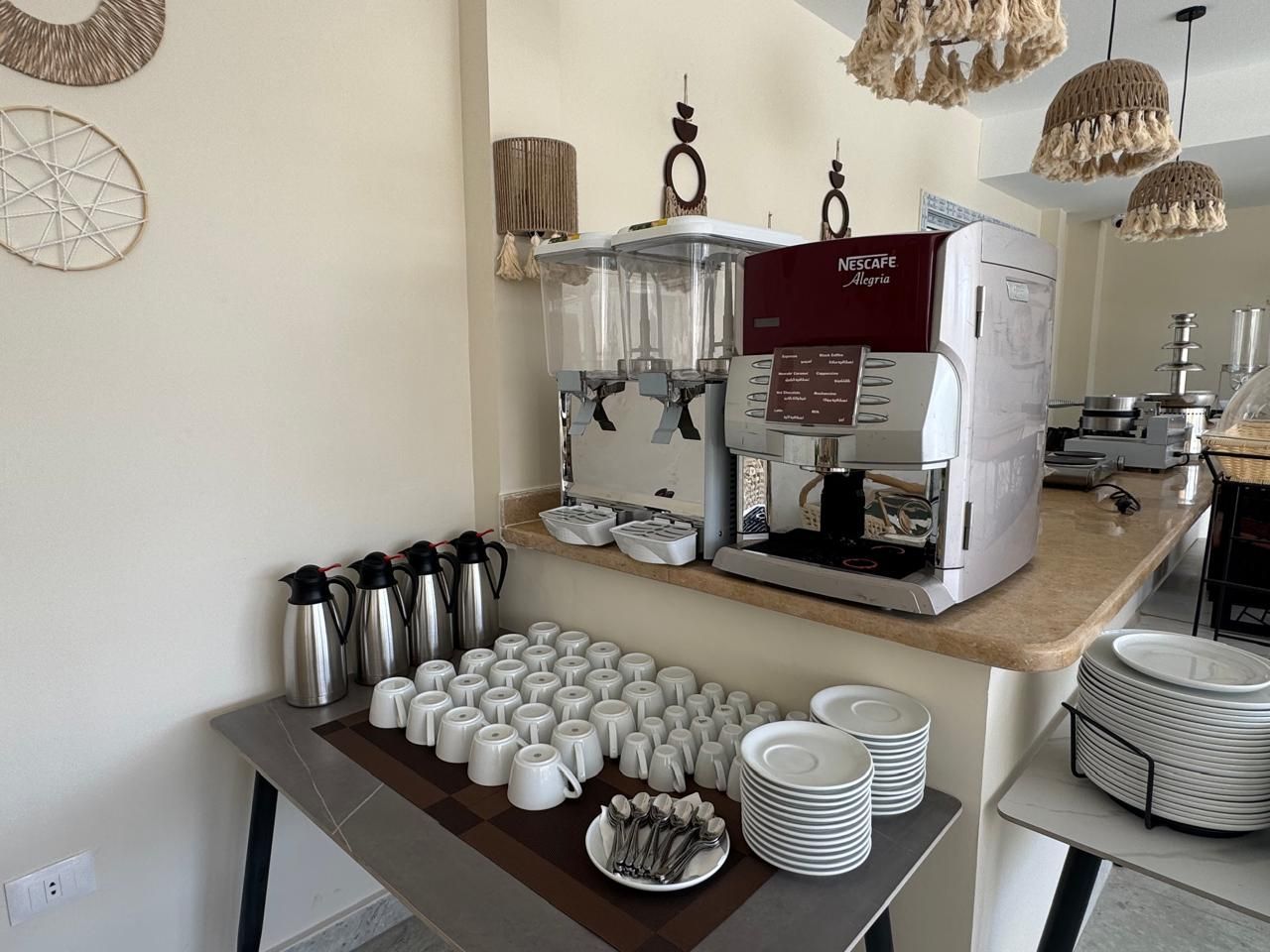 A coffee machine is sitting on a counter next to a table filled with cups and plates.