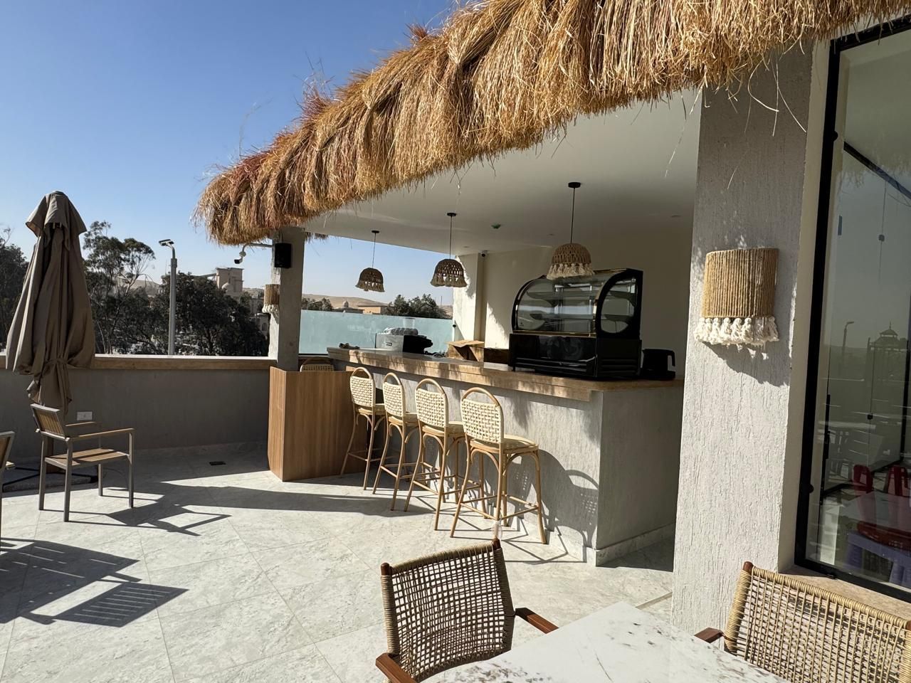 A patio with a bar and chairs under a thatched roof.