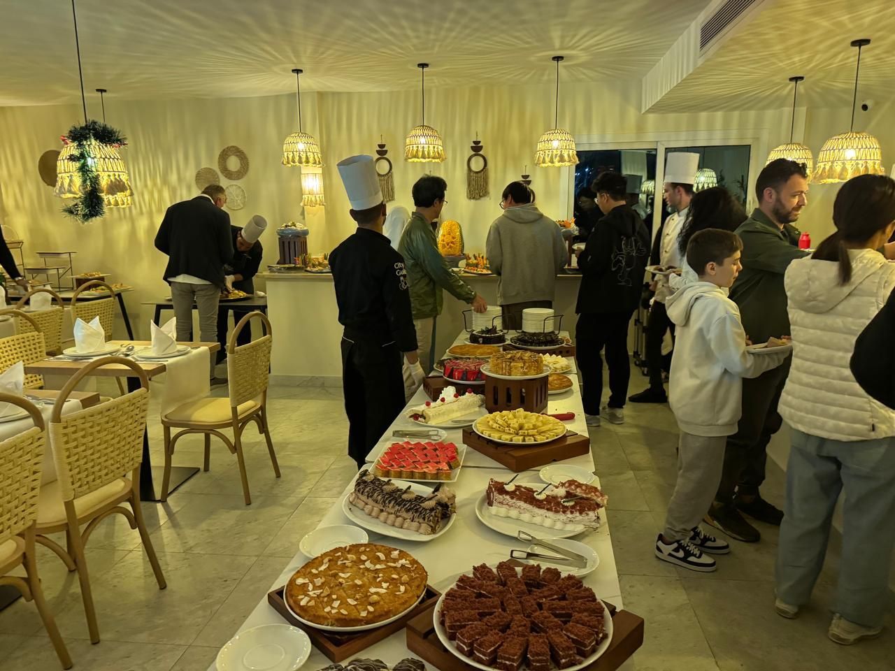 A group of people are standing around a table with a variety of desserts on it.