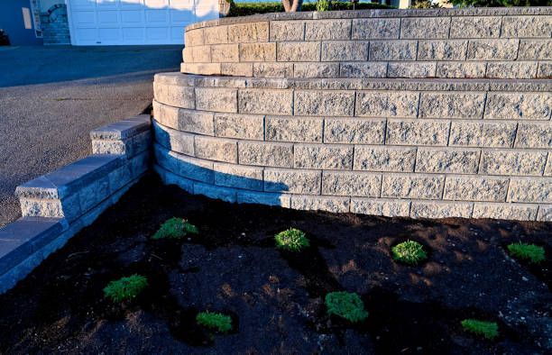 Terraced stone wall with plants, driveway and garage in background.