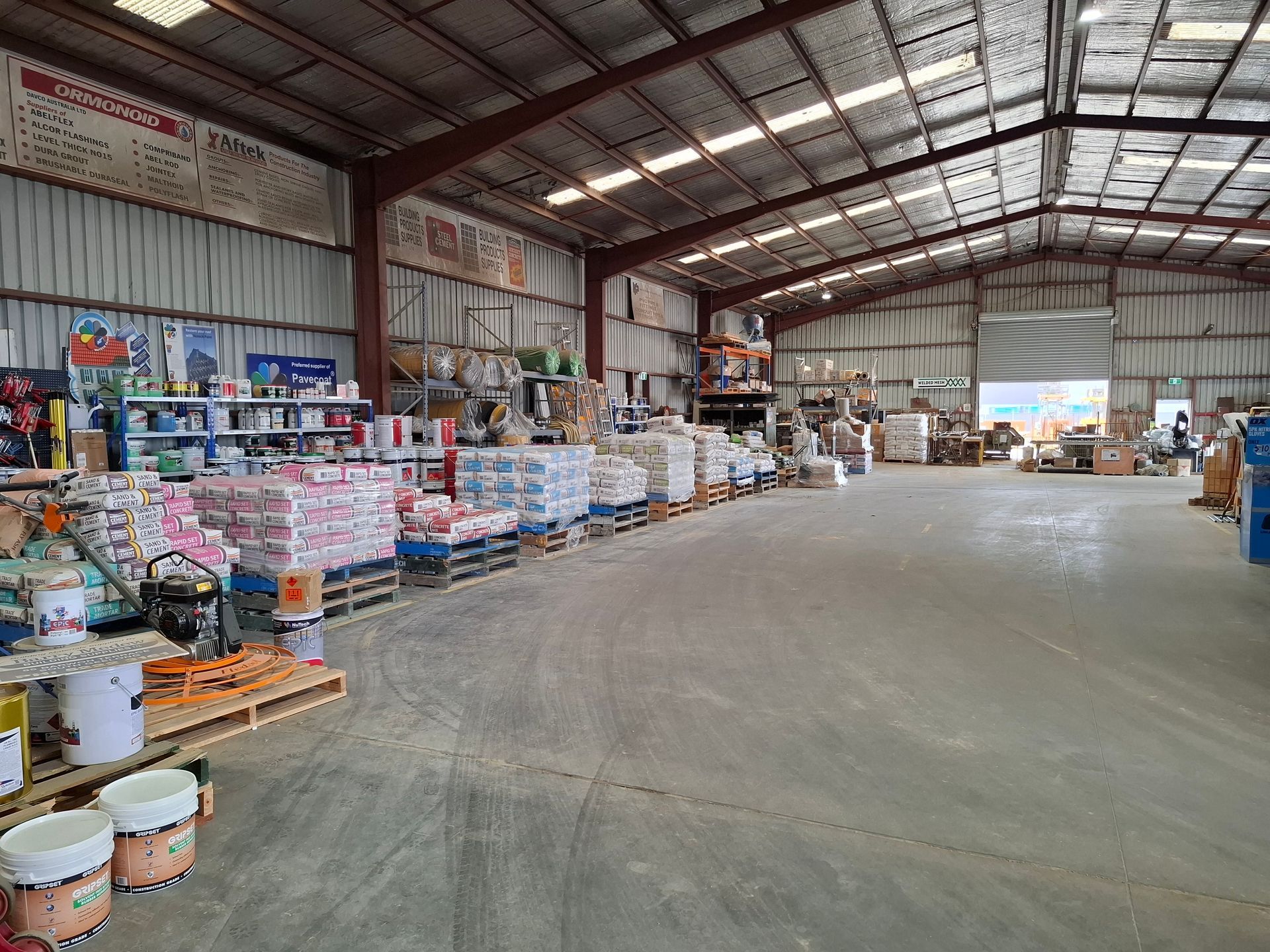 Warehouse interior with stacked supplies on pallets, including paint cans and bags.