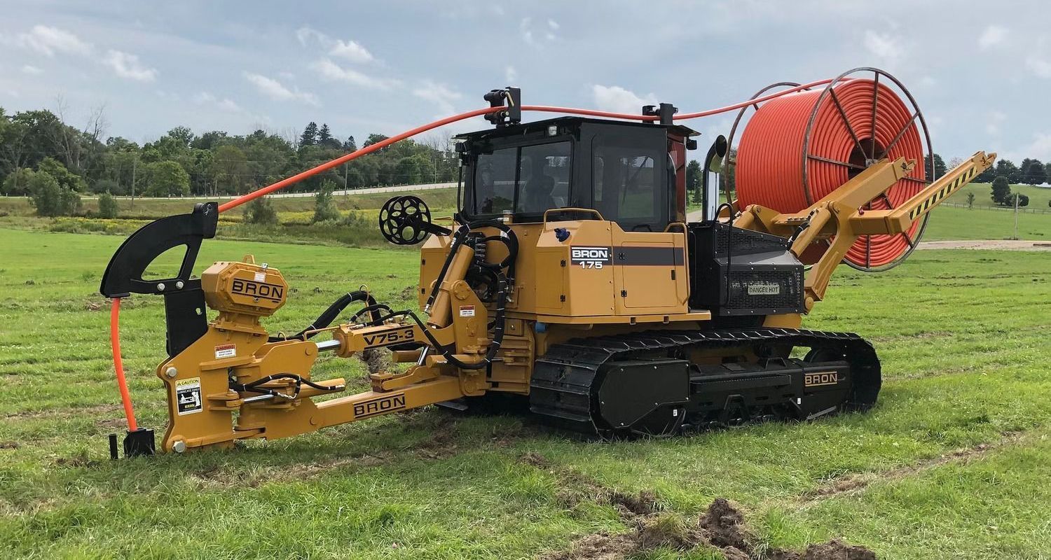 A bulldozer is sitting in a grassy field with a large orange hose attached to it.