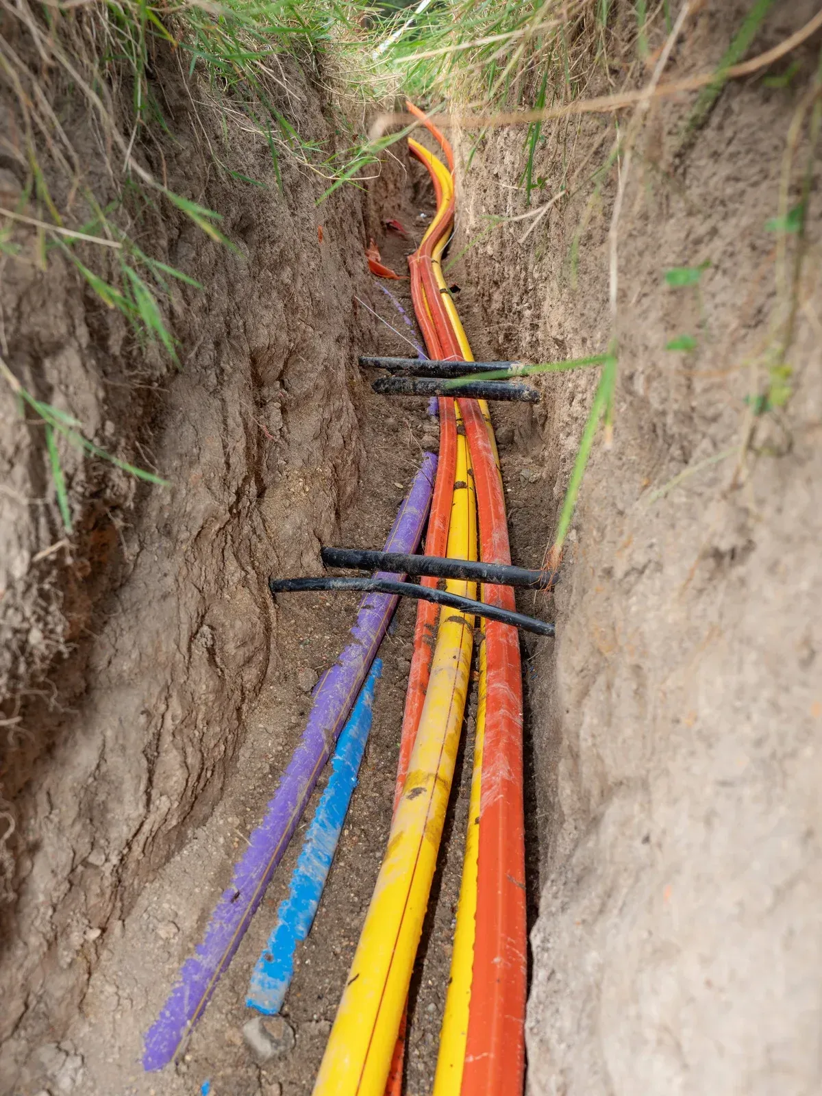 A bunch of colorful pipes are laying in a trench.