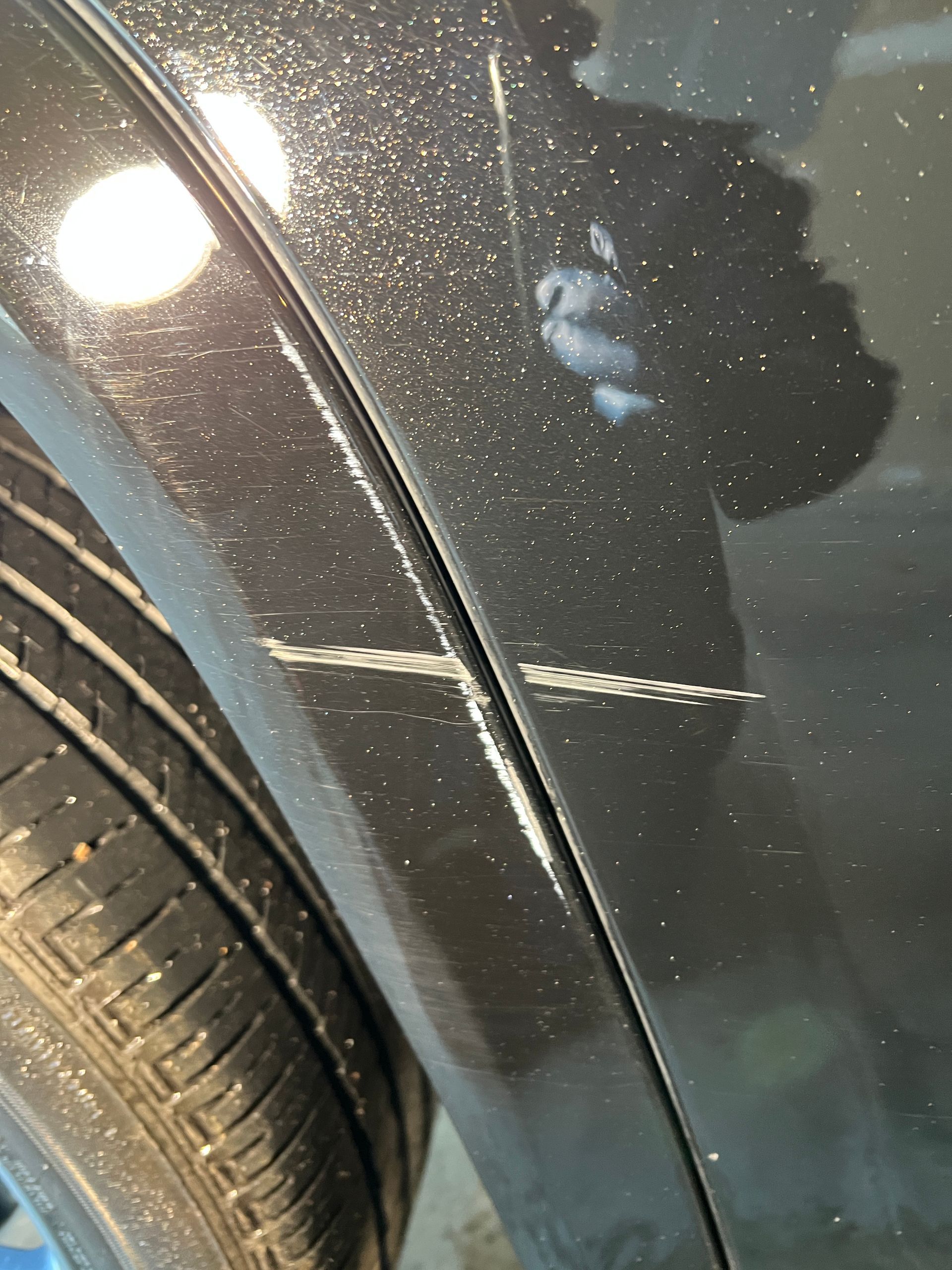 Black car body panel with long scratches, next to a tire.