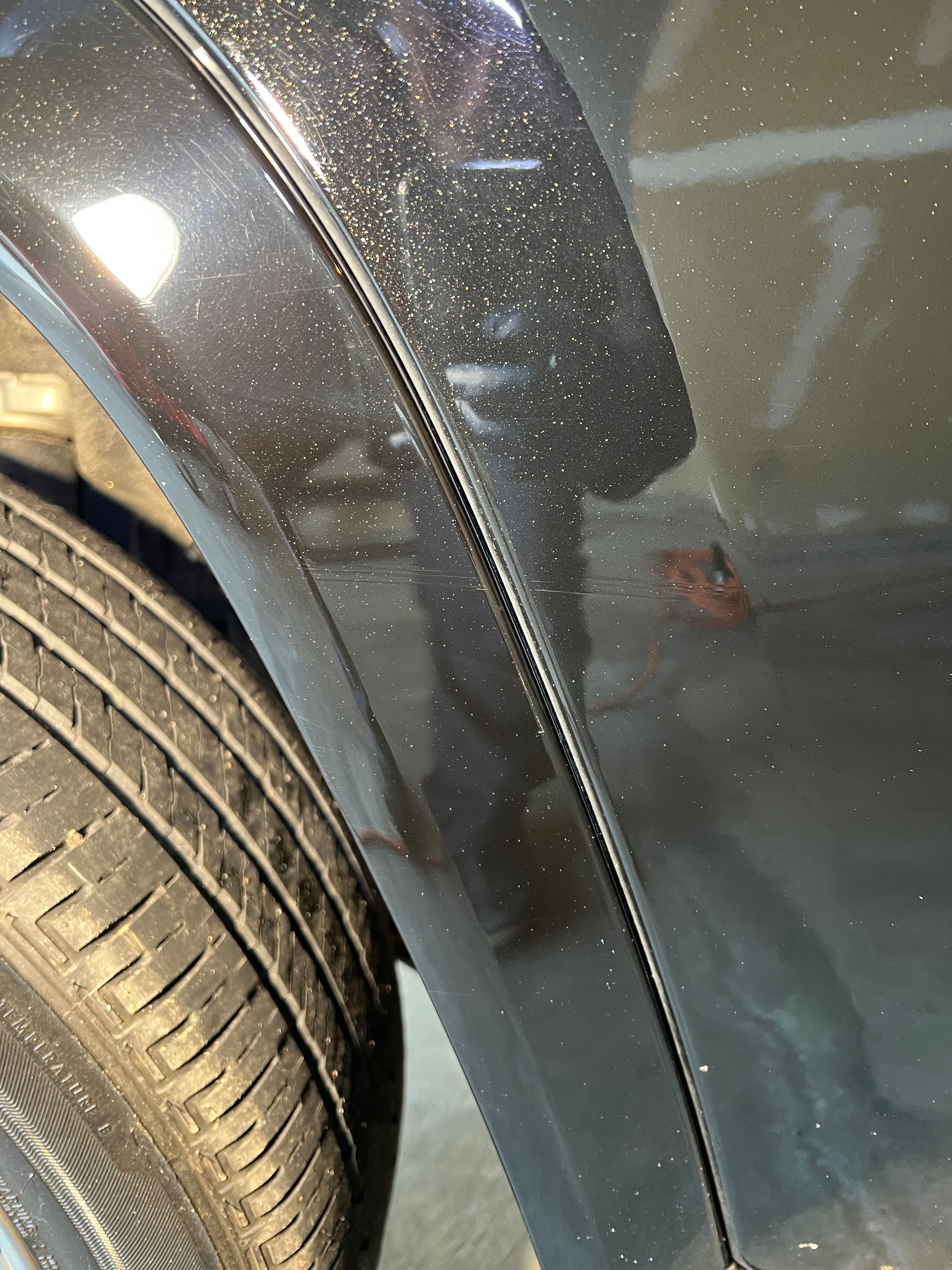 Close-up of a car's black fender near a tire. A spot of rust is visible.