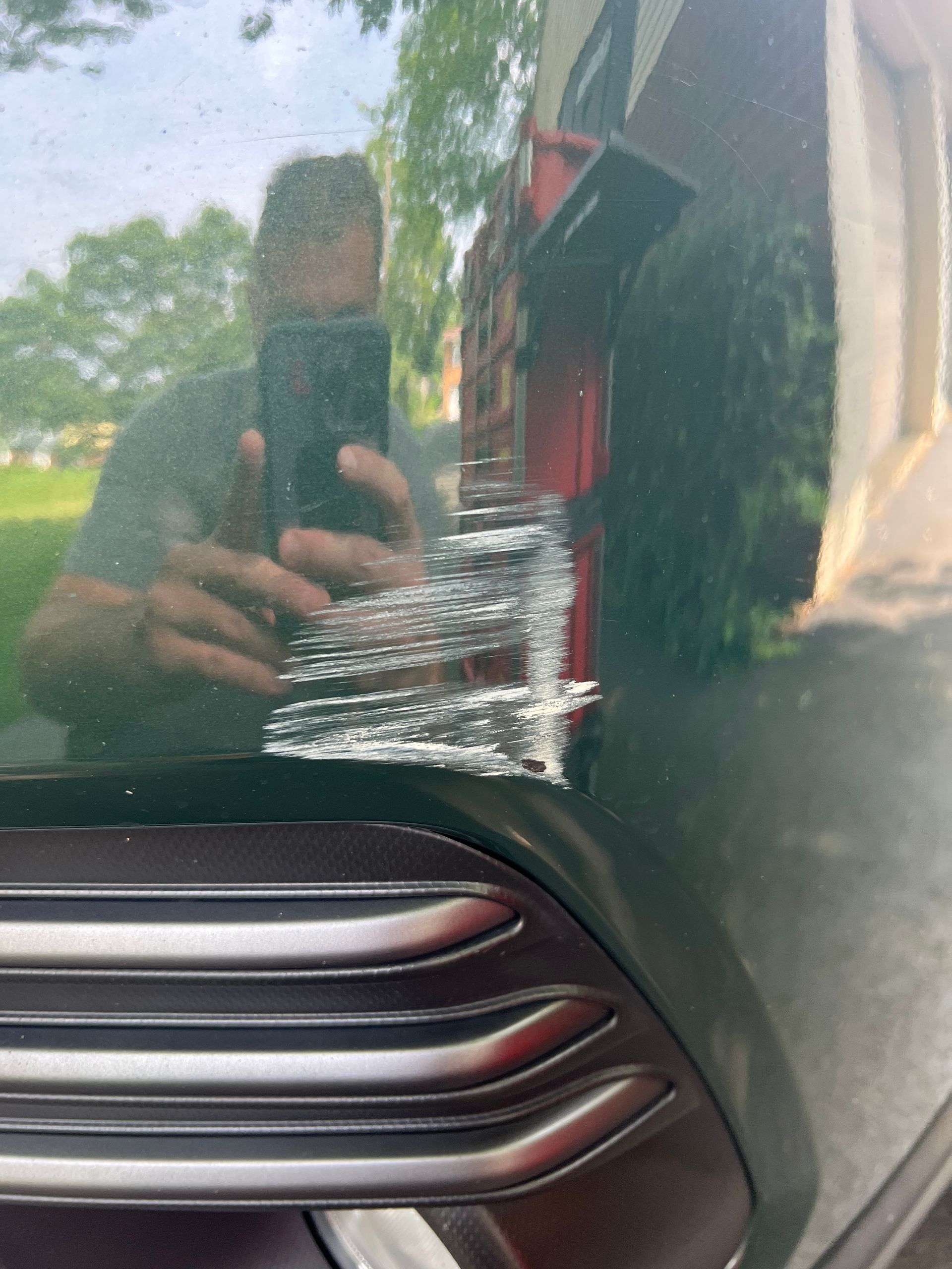 Green car panel with large scratch. Reflected person holding phone.
