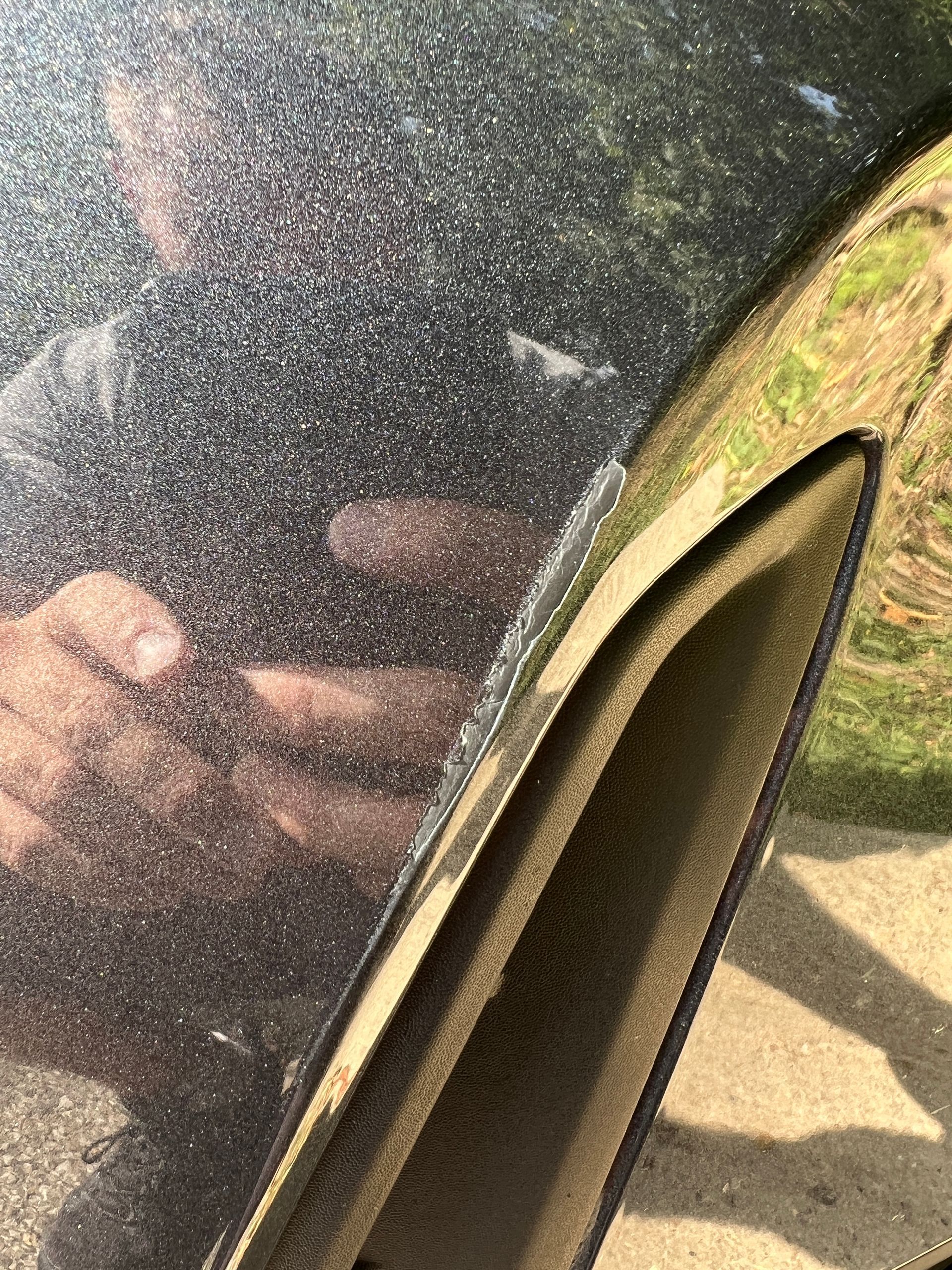 Close-up of a car's black metallic paint with damage near a black trim piece.