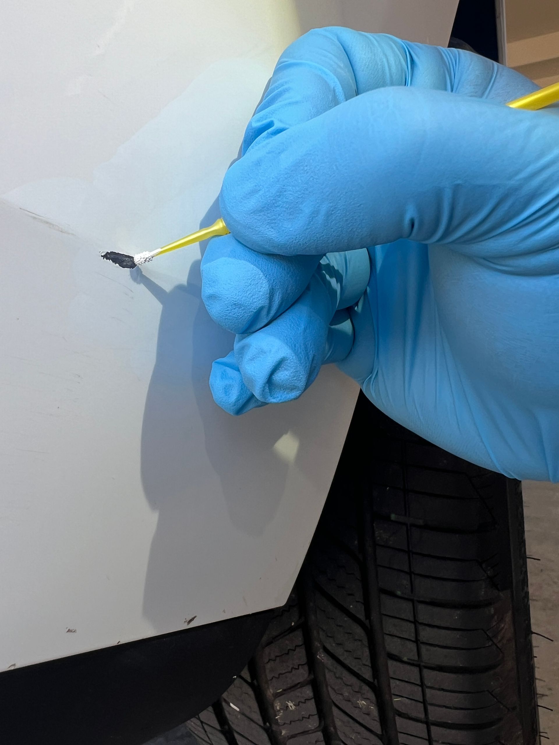 Gloved hand applying paint to a car's scratch with a fine brush.