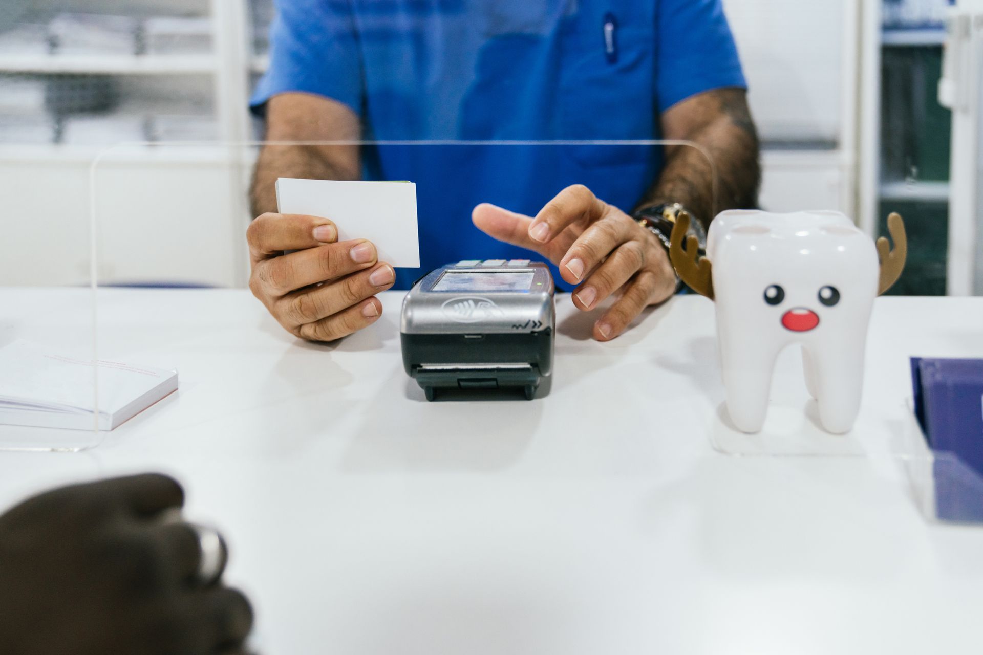 Person holding a card over a card reader at a counter, with a tooth model; dental office.