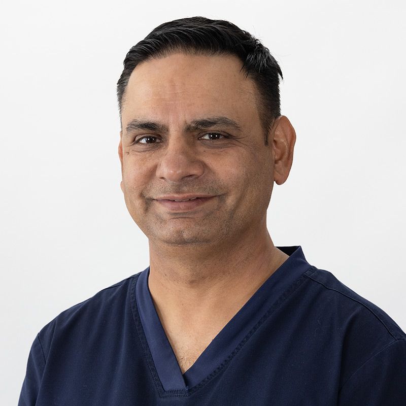 Man in blue scrubs smiling, against a white background.