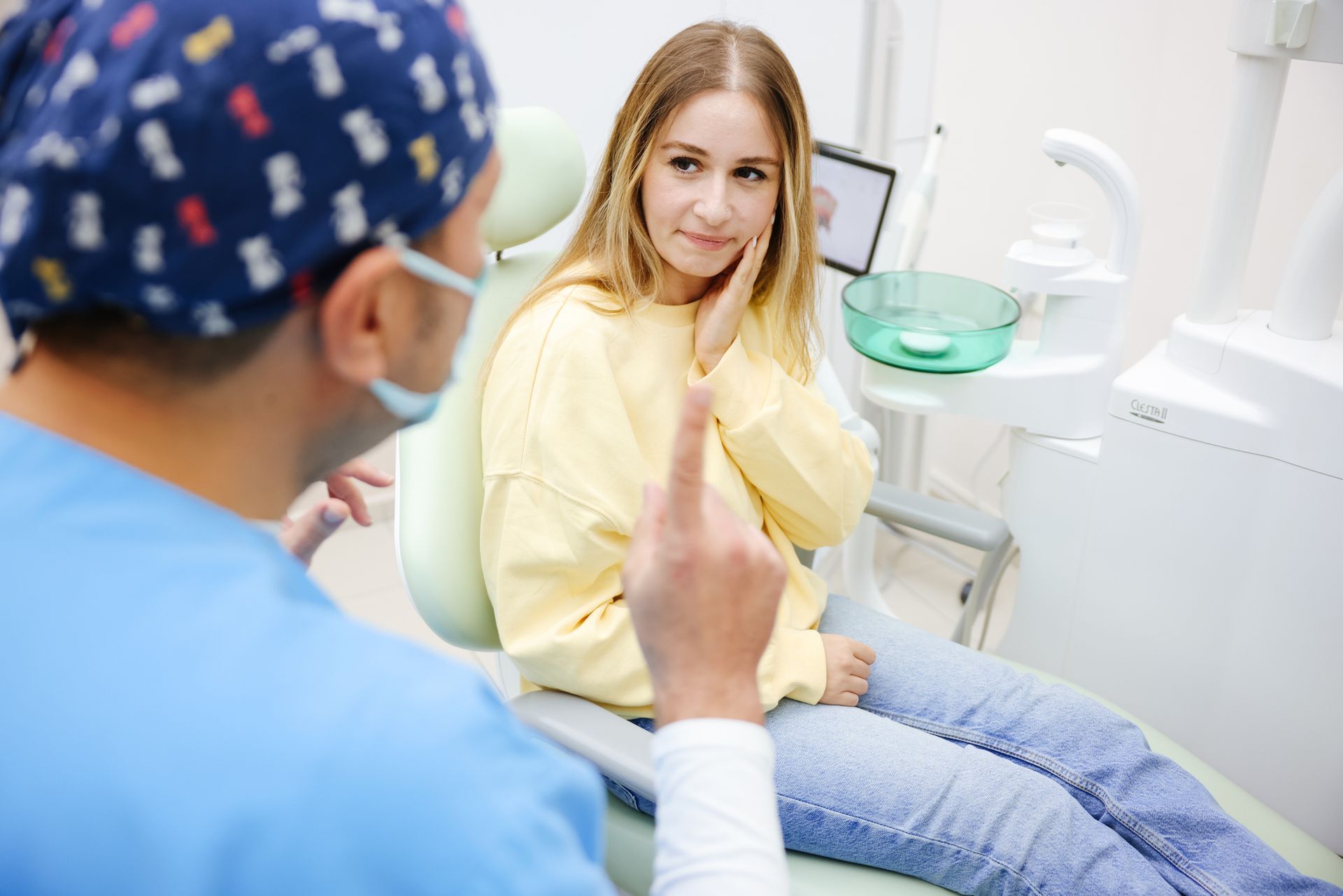 Dentist examining a woman in a dental chair, pointing at her jaw.